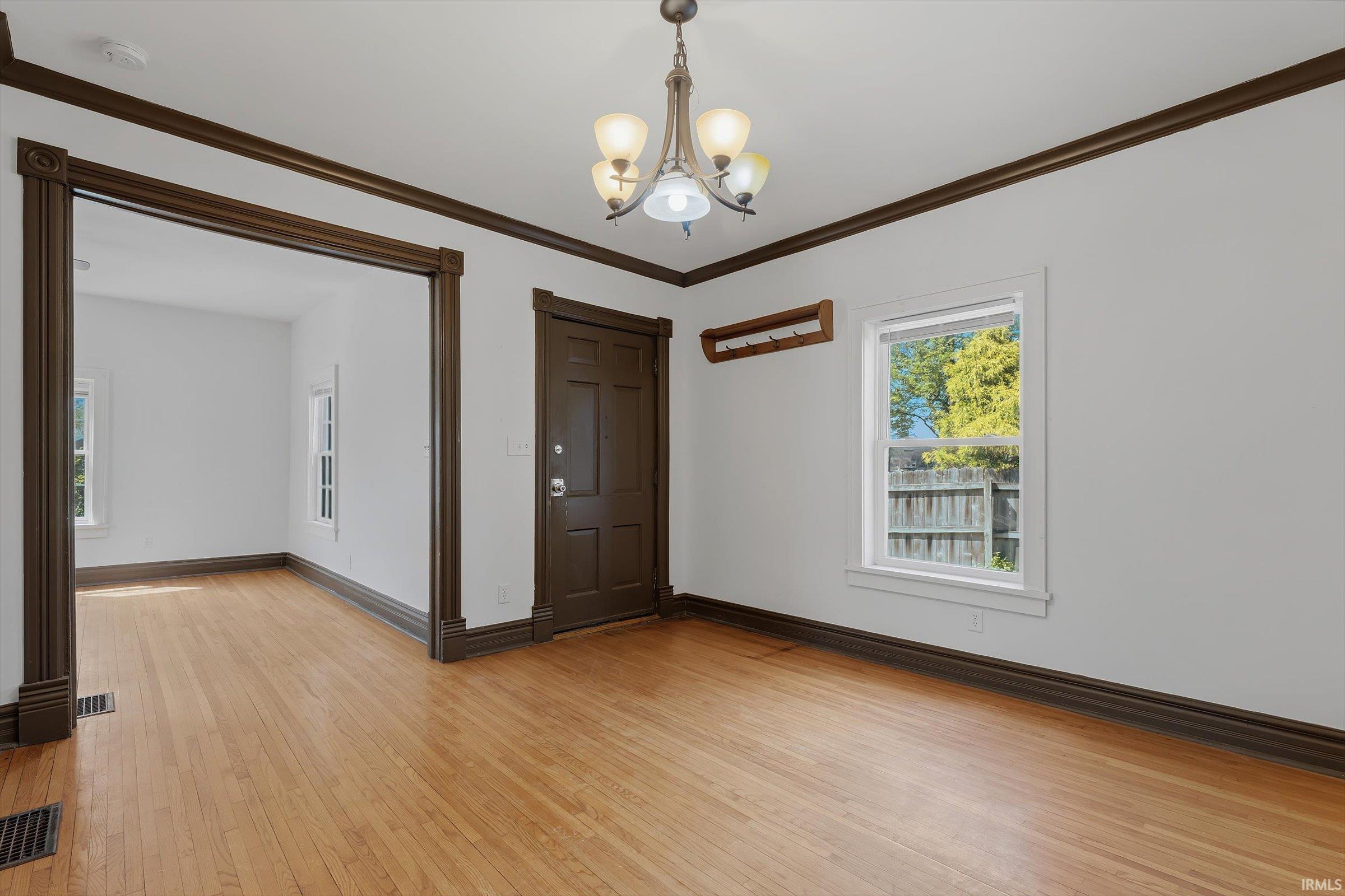 Unfurnished room featuring crown molding, hanging lights, and light wood-style flooring