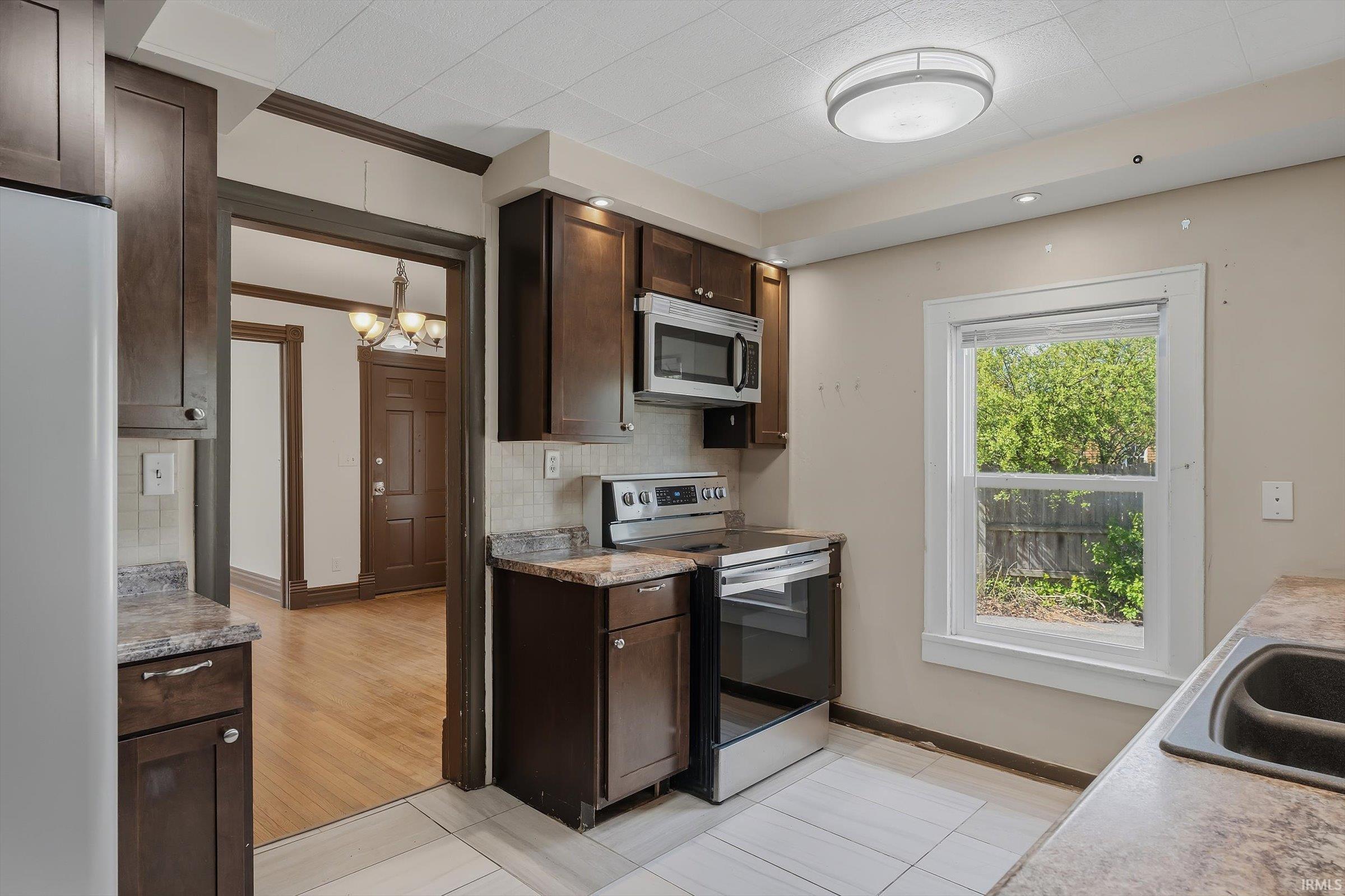 Kitchen featuring dark wood finish cabinets, stainless steel appliances, tasteful backsplash, light countertops, and crown molding