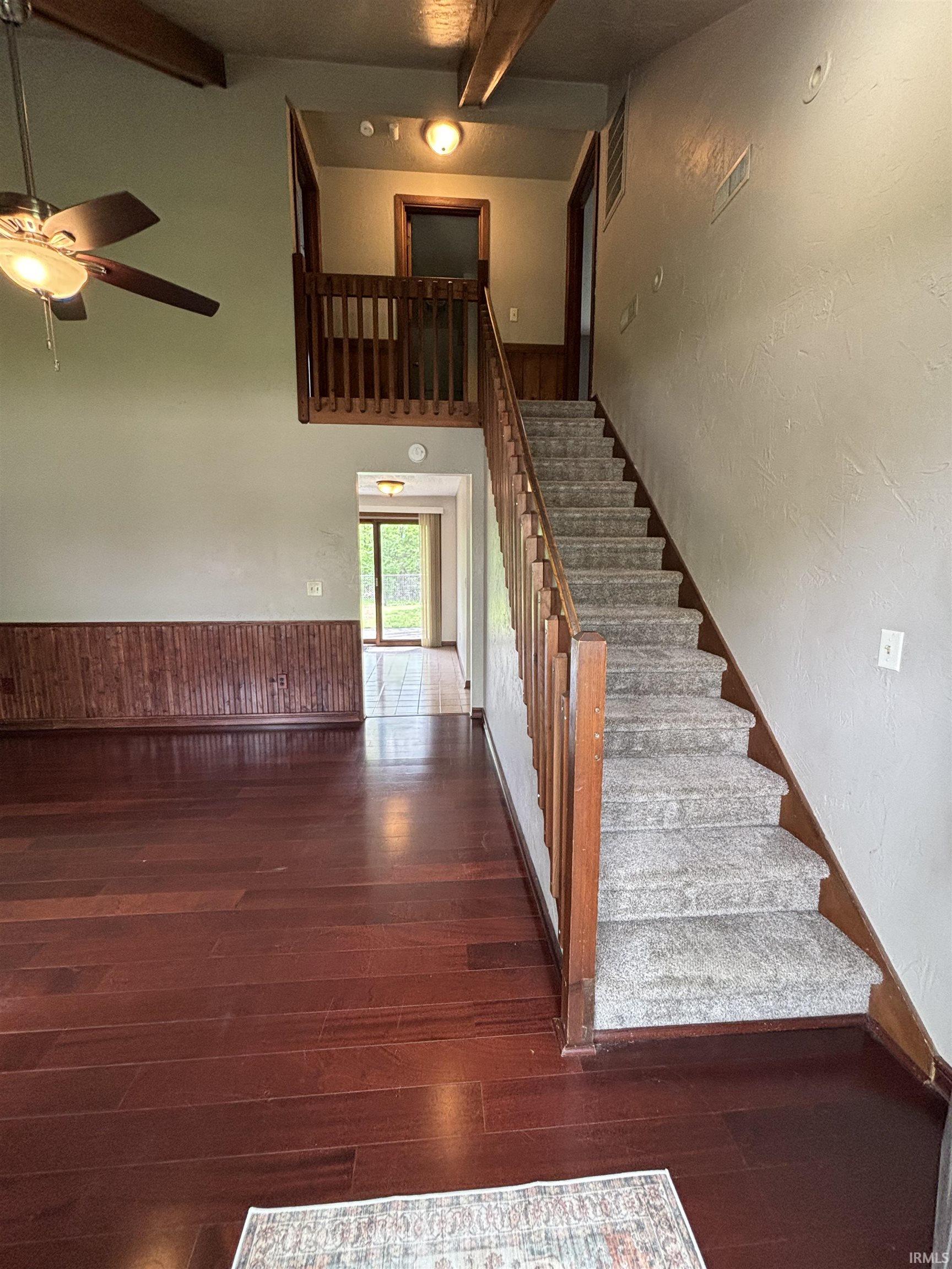 Staircase featuring a ceiling fan, hardwood / wood-style flooring, wainscoting, wood walls, and a textured wall