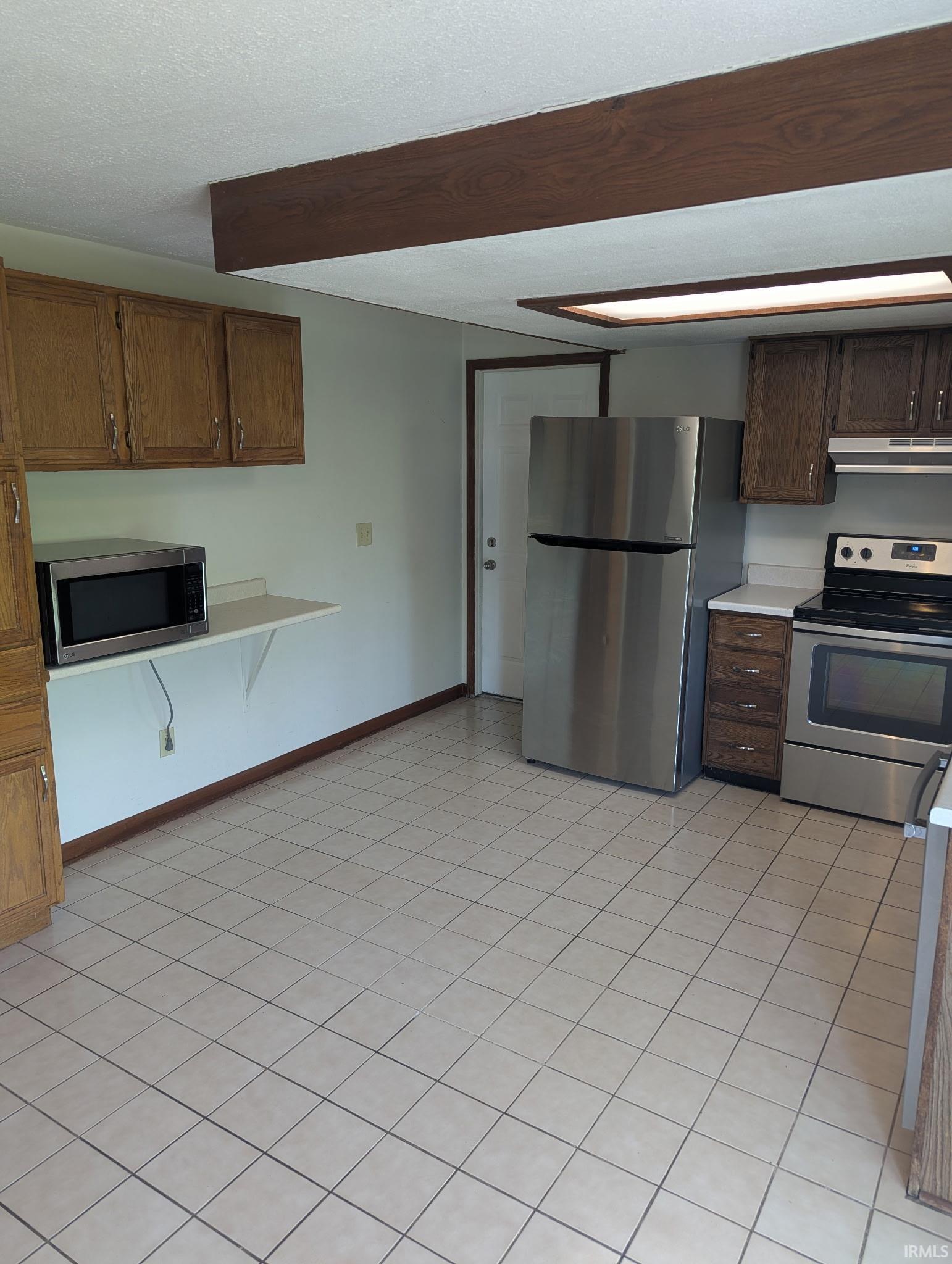 Kitchen with stainless steel appliances, light countertops, light tile patterned flooring, and a textured ceiling