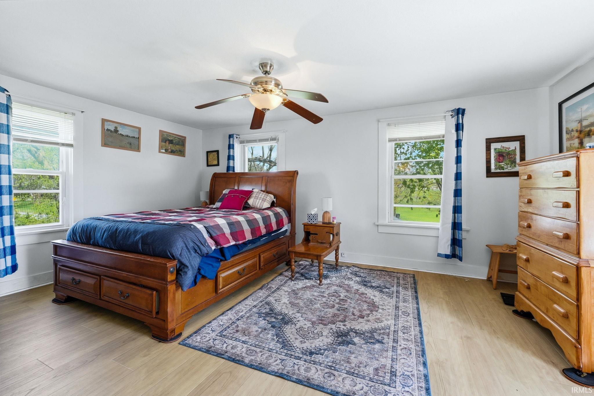 Light wood-finish flooring provides a bright base for this room featuring a ceiling fan with light, multiple windows, and white walls