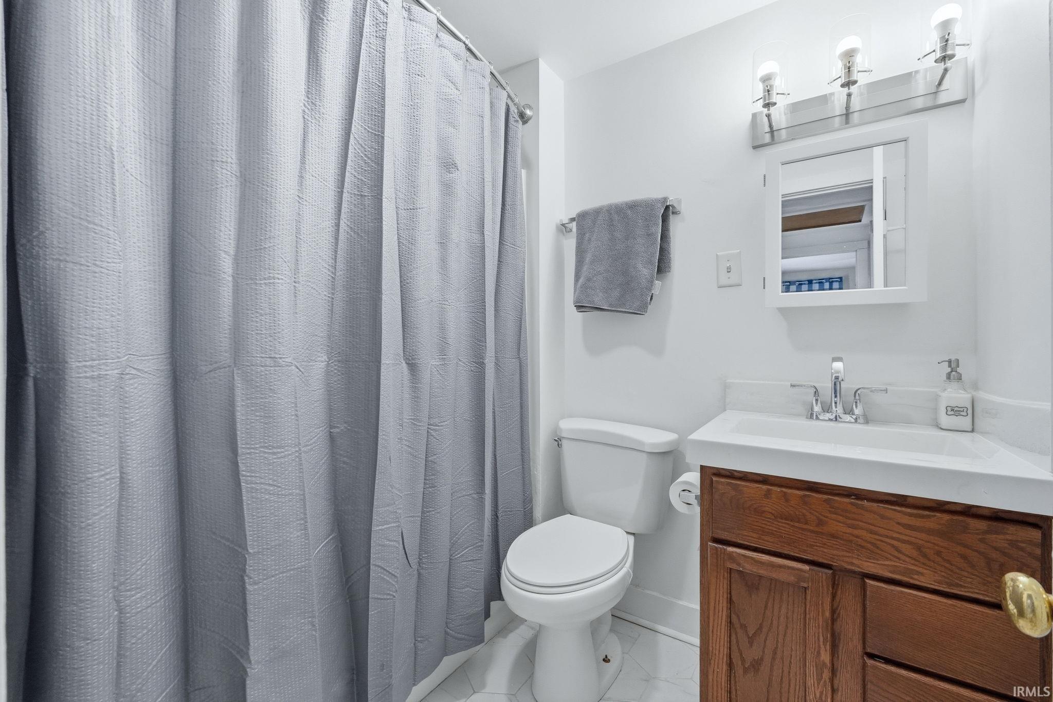 Bathroom featuring a white toilet, wood-finish vanity with a white countertop, chrome faucet, and a wall-mounted mirror with integrated lighting