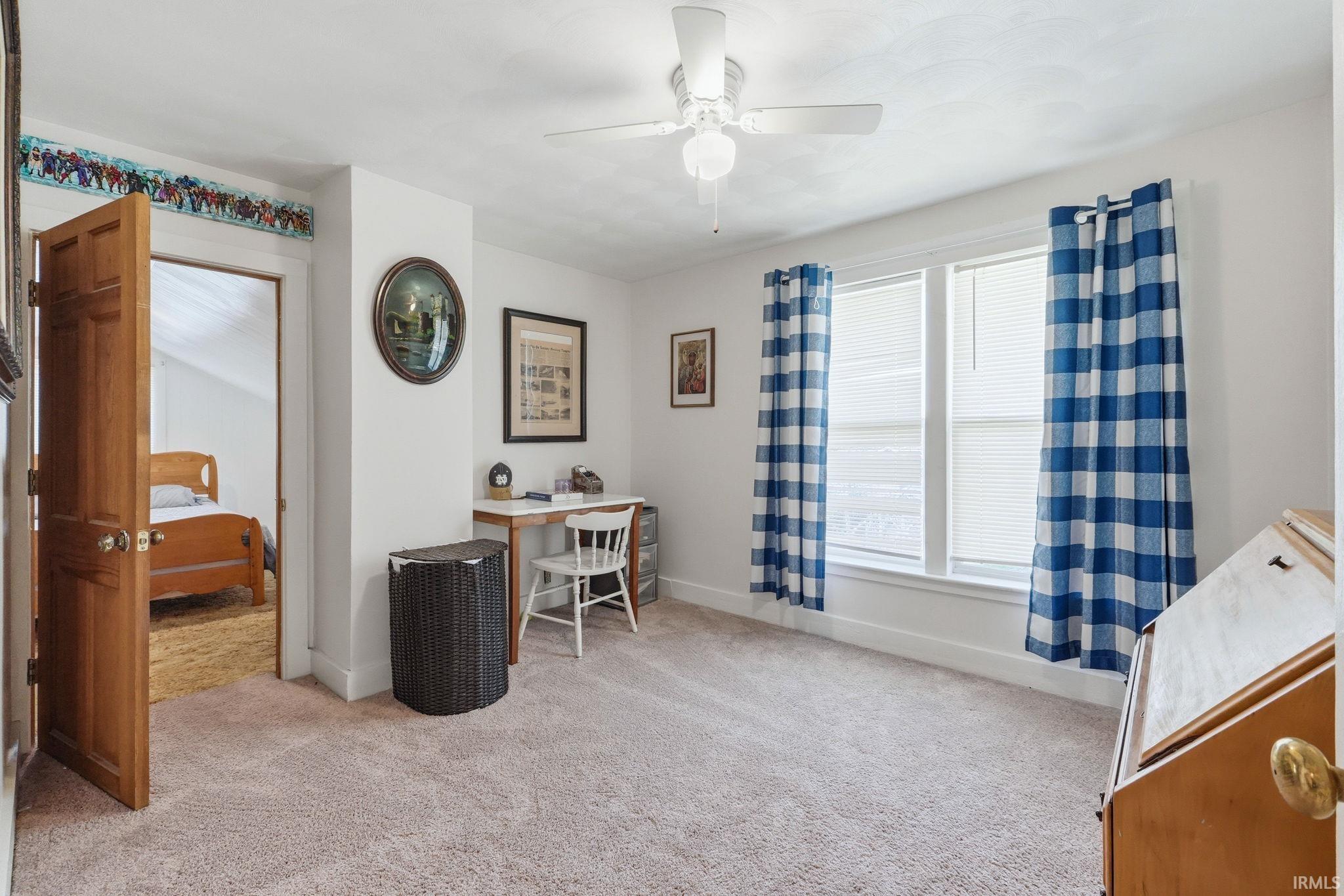 Carpeted room featuring a ceiling fan with light fixture, two windows with blinds, and a solid wood door