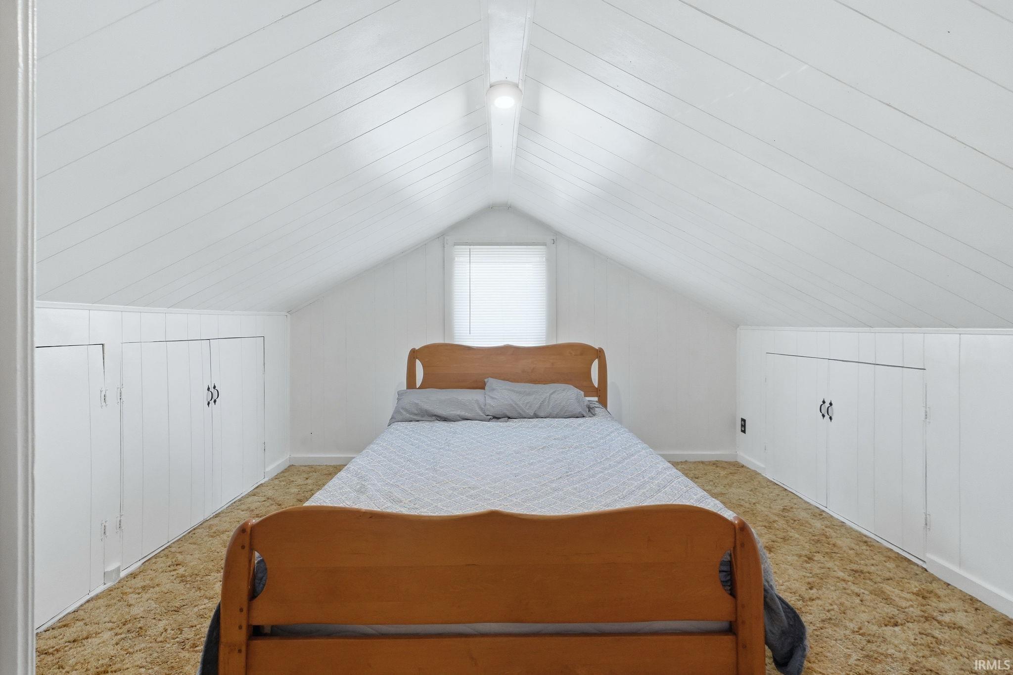 Attic space featuring sloped wood-paneled ceilings, white wall finishes, built-in storage cabinets with black hardware, and a single window