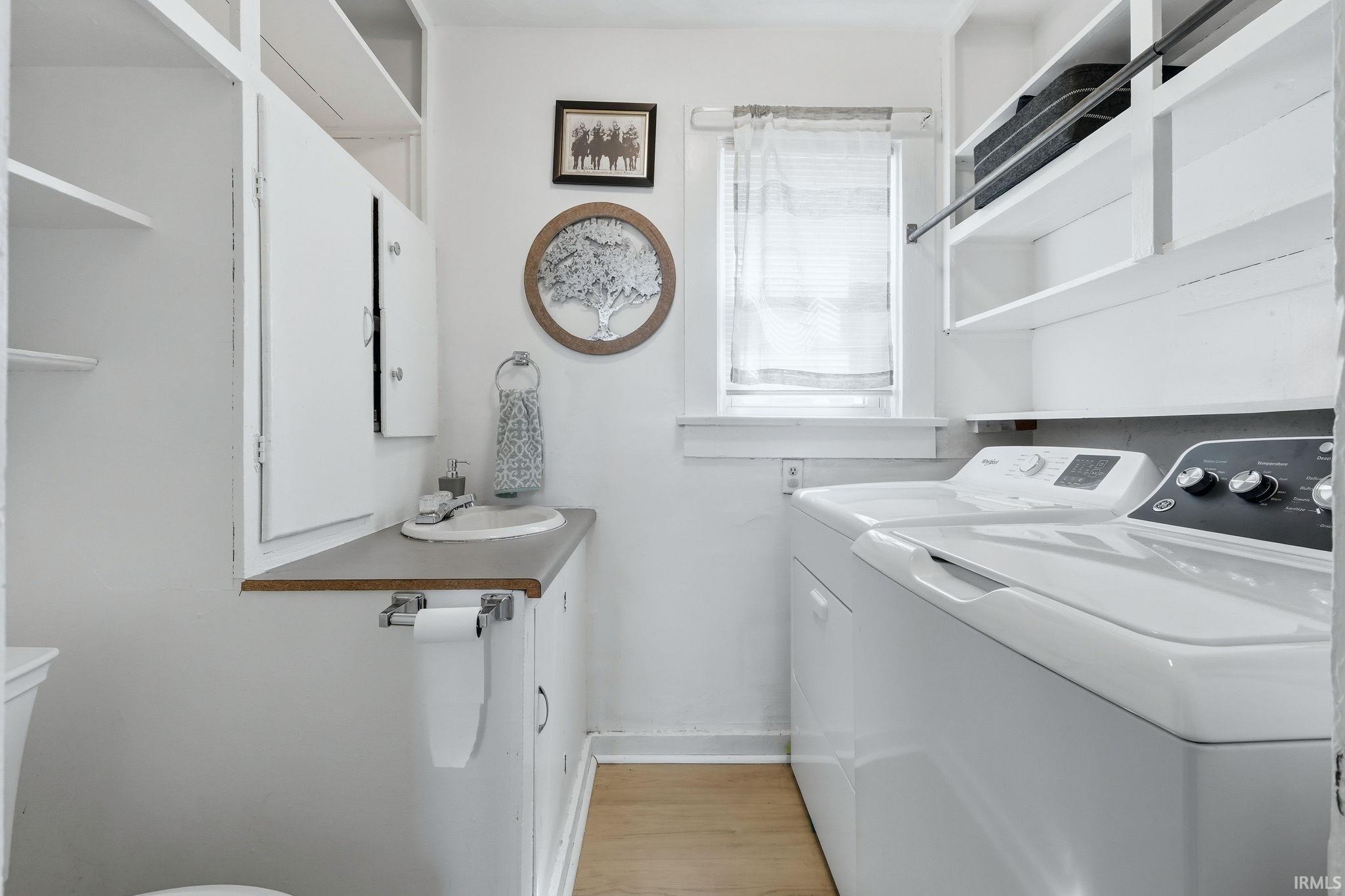 Utility room featuring wood-finish flooring, built-in shelving, a window with natural light, a vanity with an integrated sink, and white cabinetry
