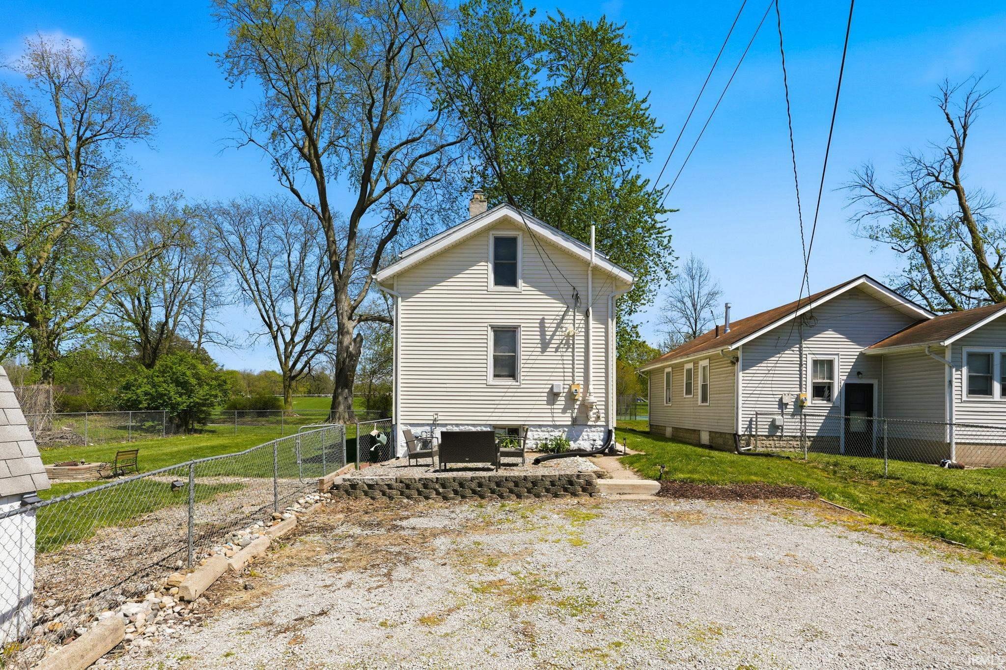Rear exterior with light-colored siding, a small concrete patio, and a retaining wall