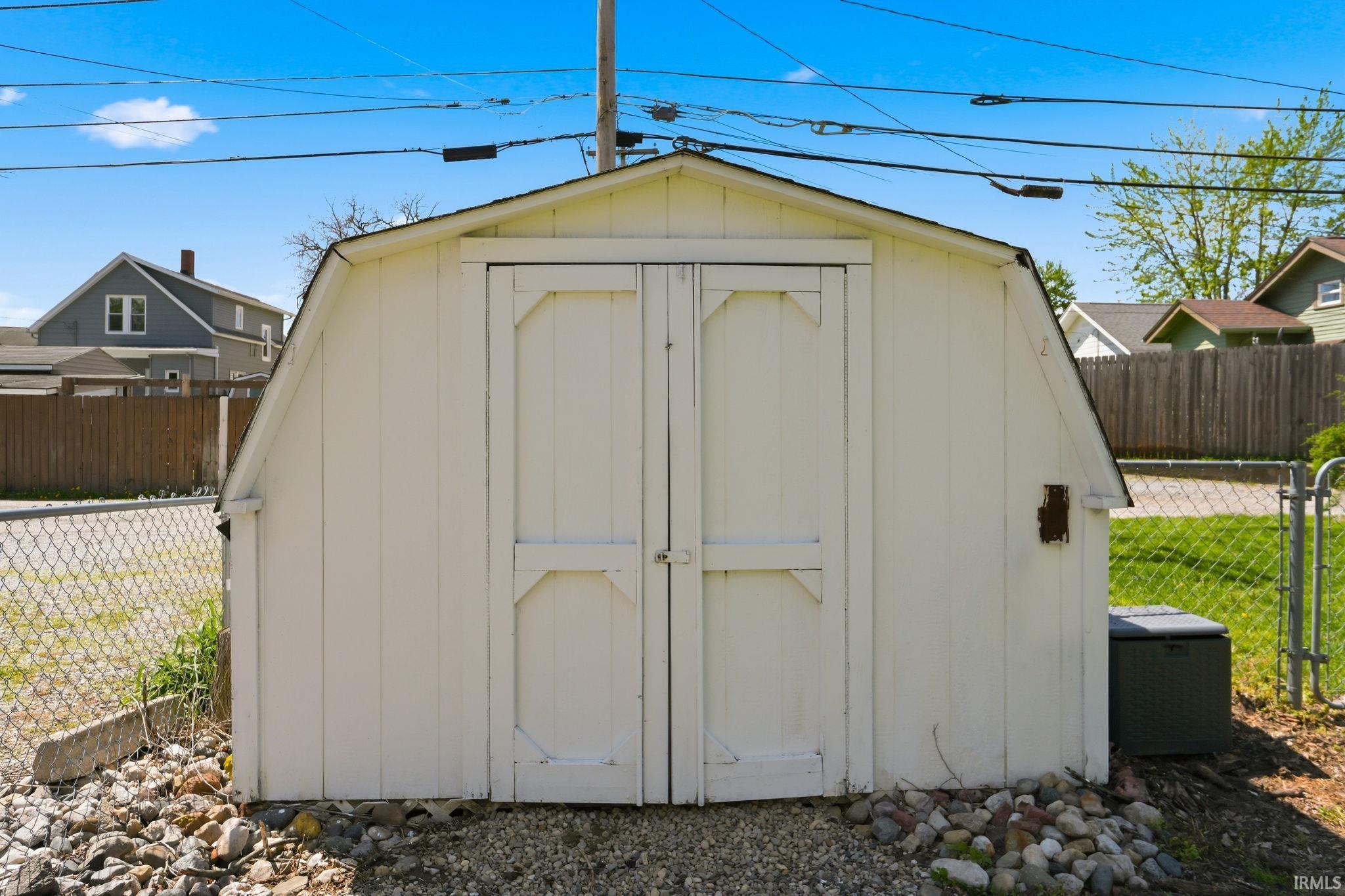 White gambrel-roof shed featuring double barn-style doors and a gravel base