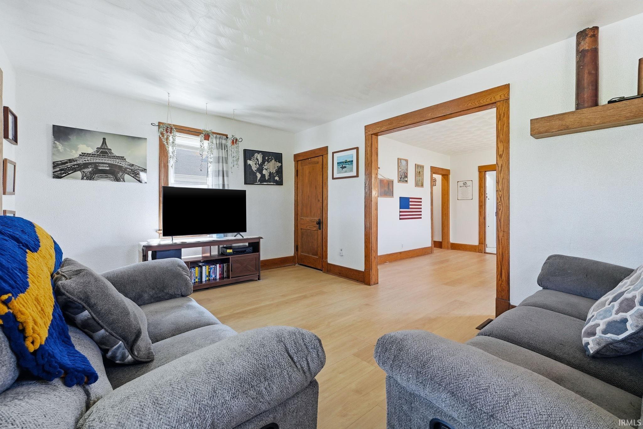 Living area with light-toned wood-finish flooring, white walls, and wood trim around doorways
