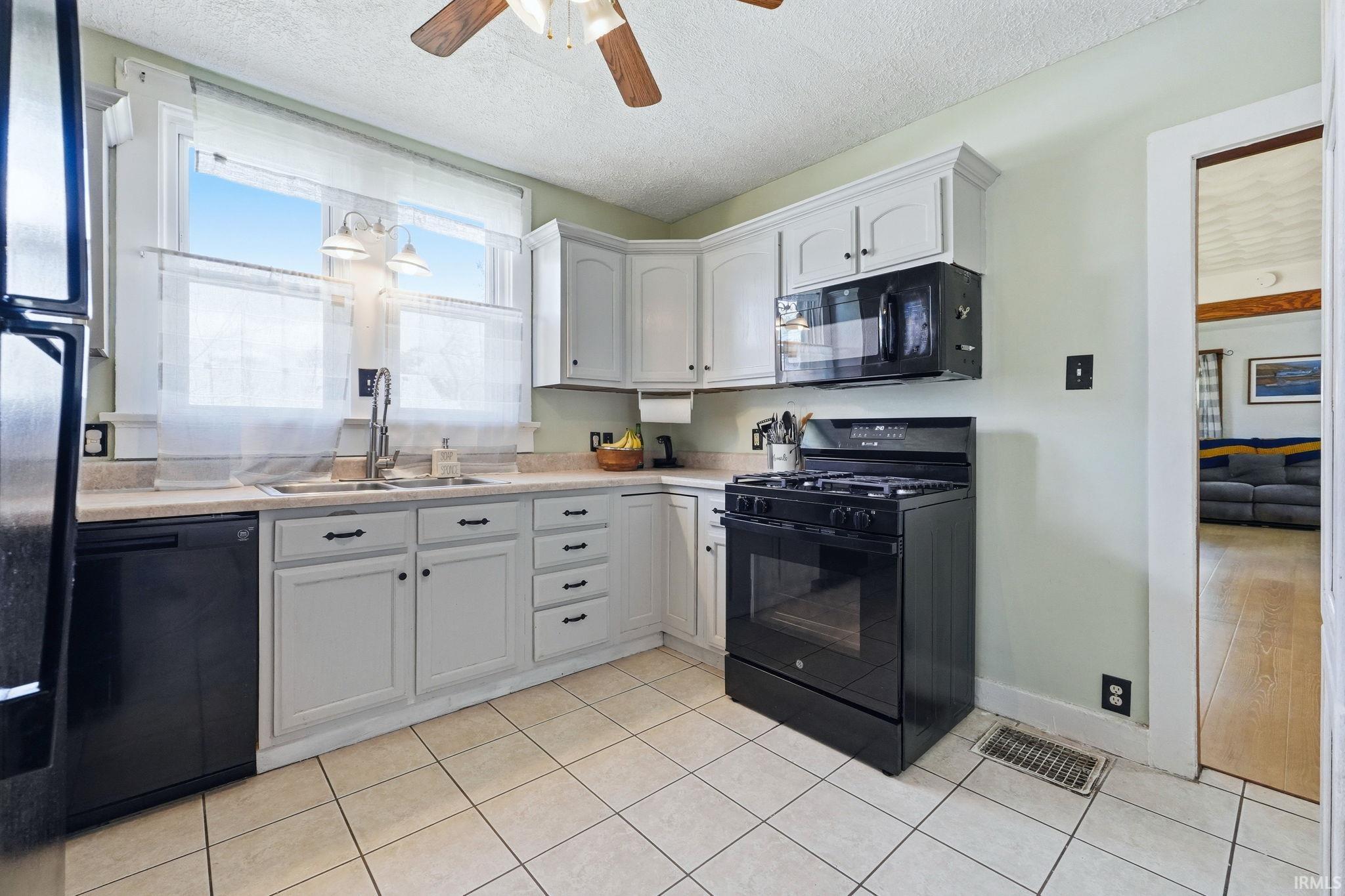 Kitchen featuring light-toned cabinetry, a black range with an overhead microwave, and a black dishwasher