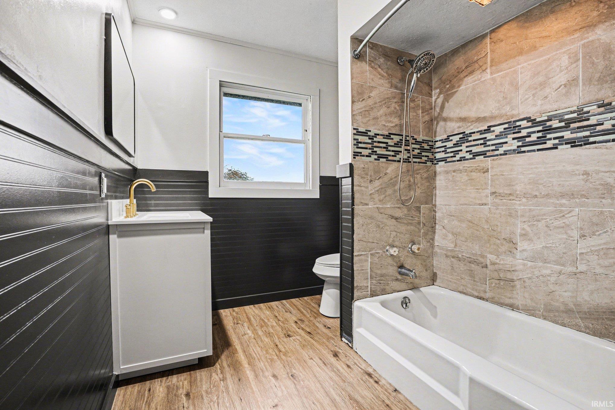 Full bath featuring vanity, wainscoting, light wood finished floors, tub / shower combination, and tile walls