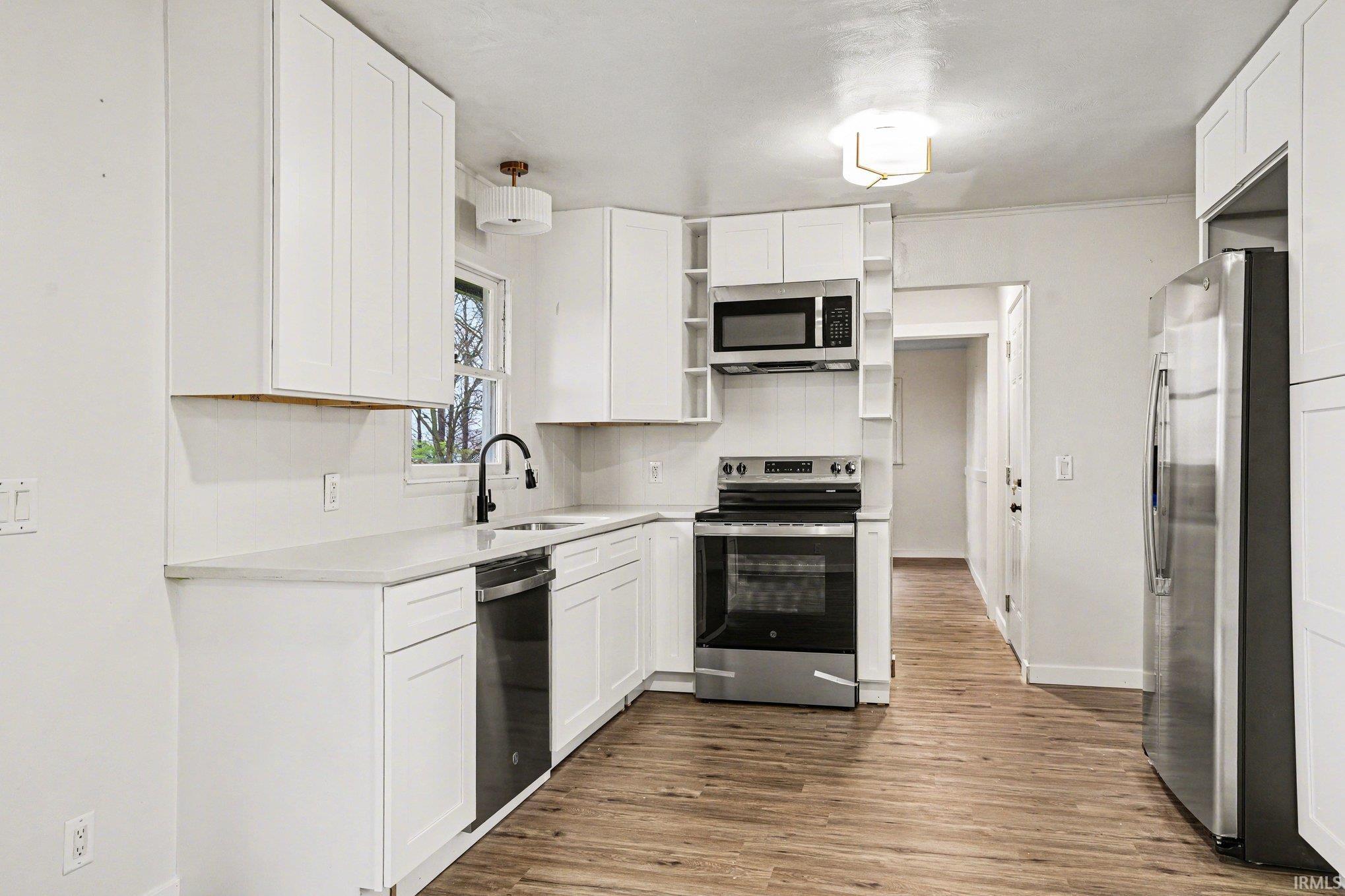 Kitchen featuring stainless steel appliances, white cabinetry, open shelves, dark wood-style flooring, and crown molding