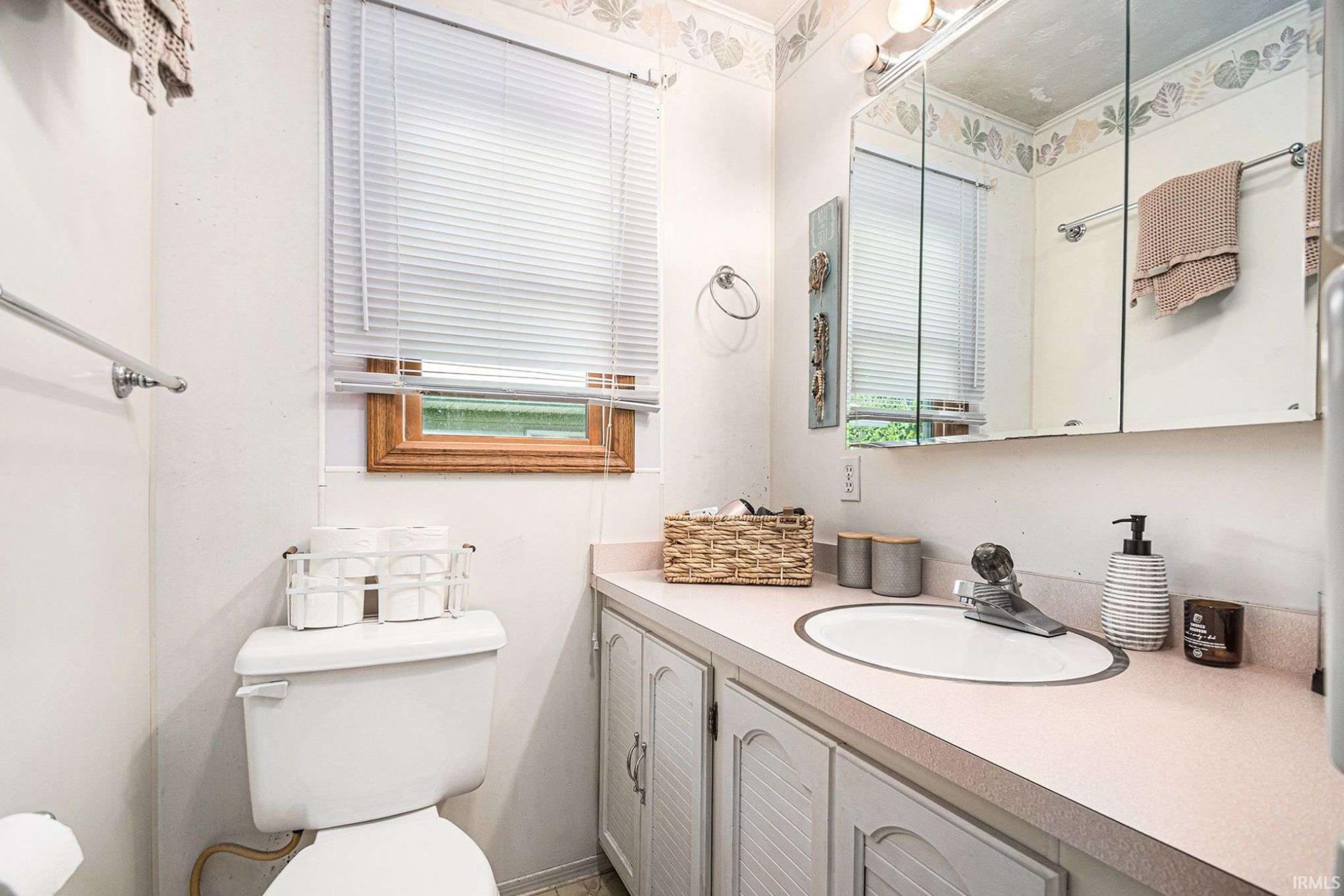Bathroom featuring a vanity with an integrated sink, a medicine cabinet with mirrored doors, and a window with wood trim