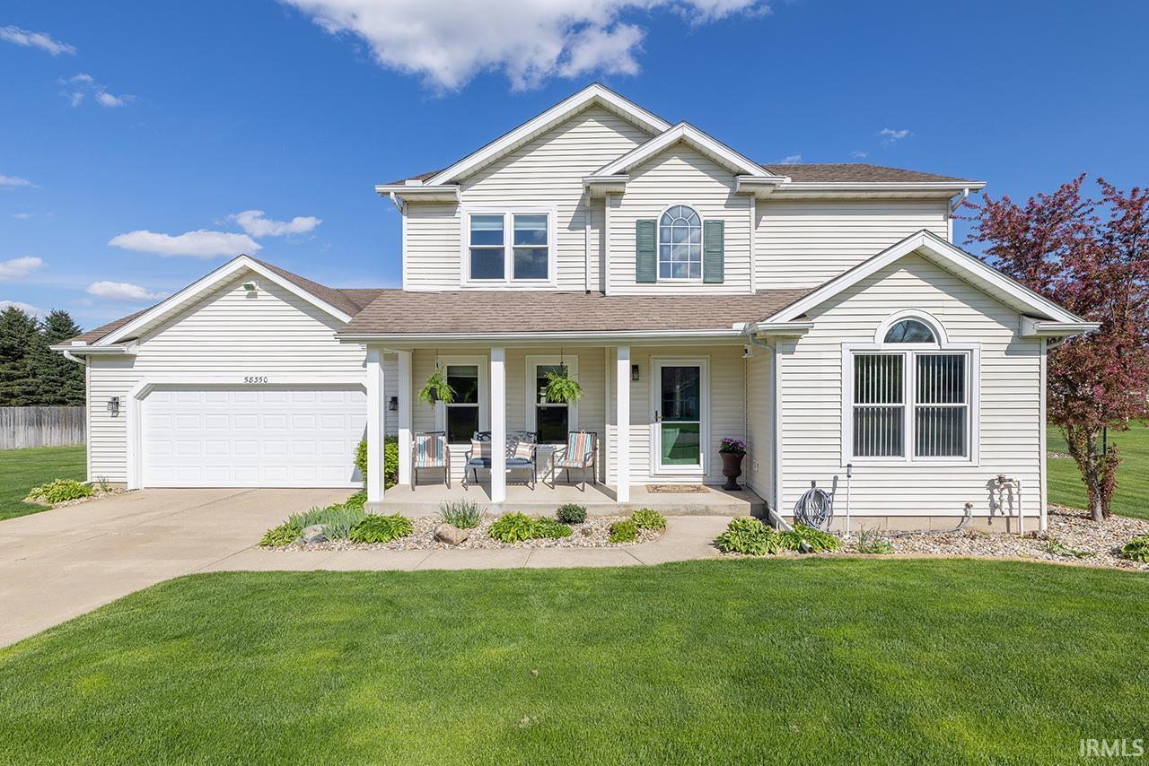 Traditional-style home with a porch, a front yard, driveway, roof with shingles, and a garage