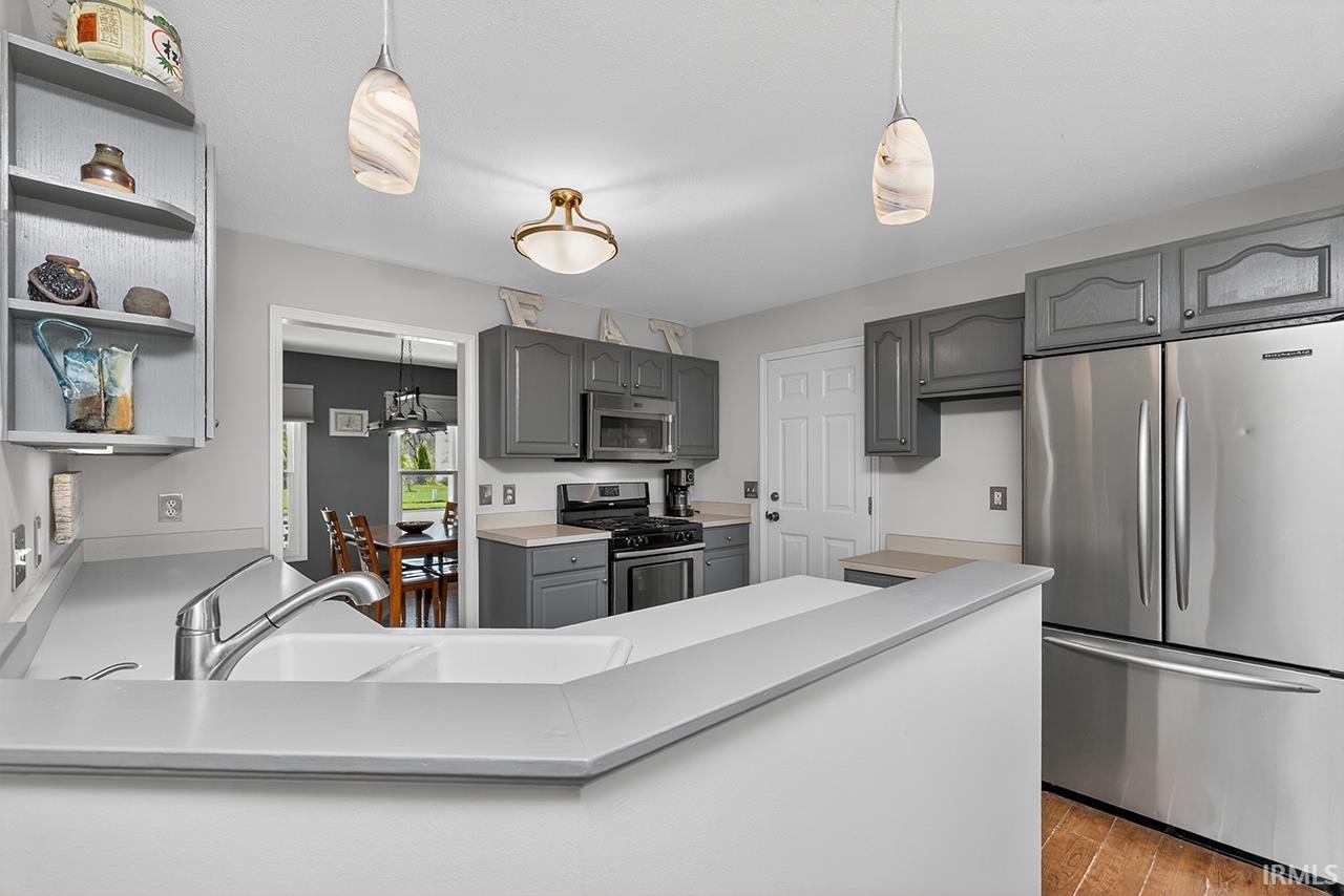 Kitchen with gray cabinetry, stainless steel appliances, decorative light fixtures, and a peninsula