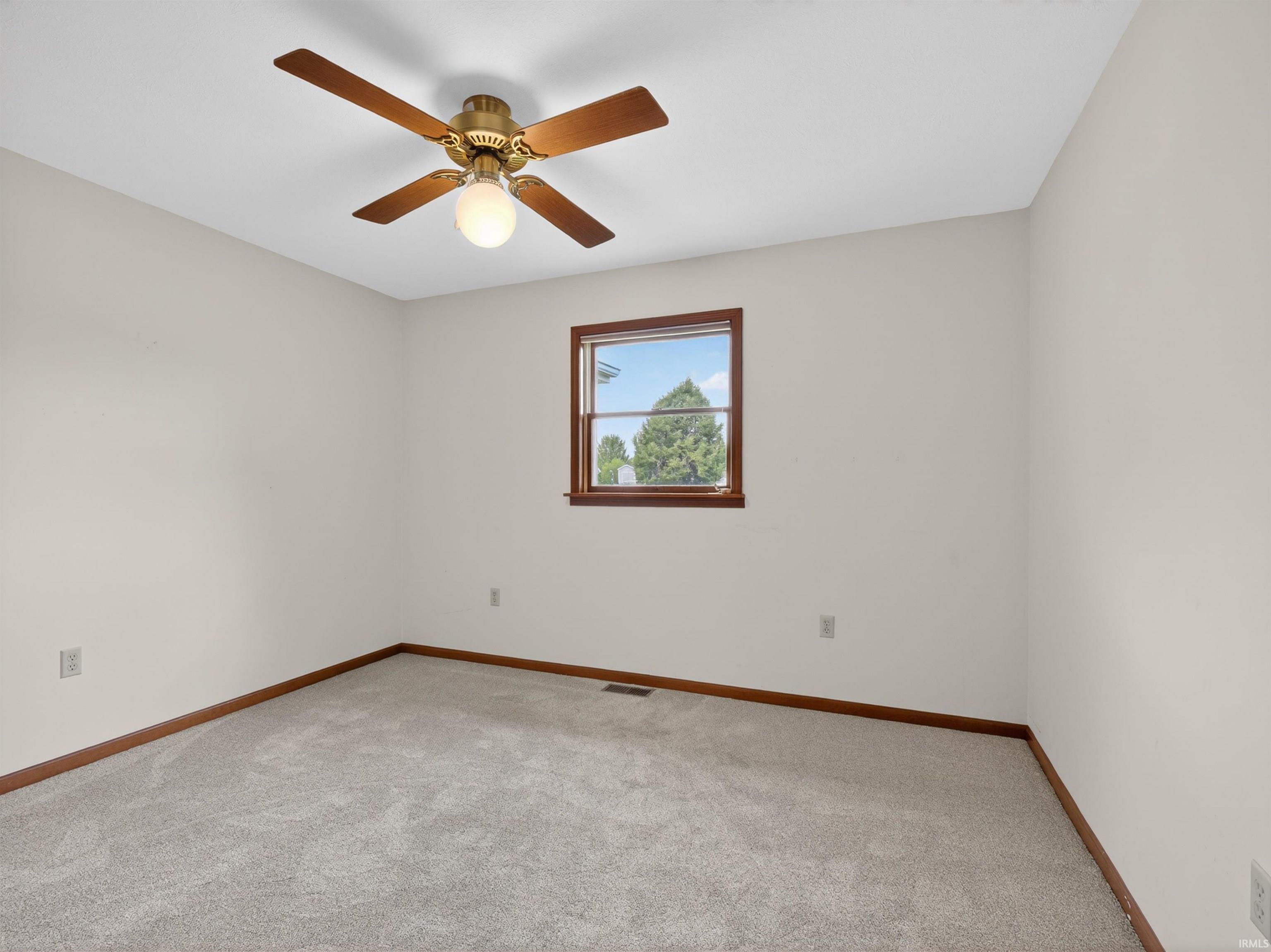 Carpeted room featuring a single window with wood trim, a ceiling fan with light fixture, and neutral wall paint
