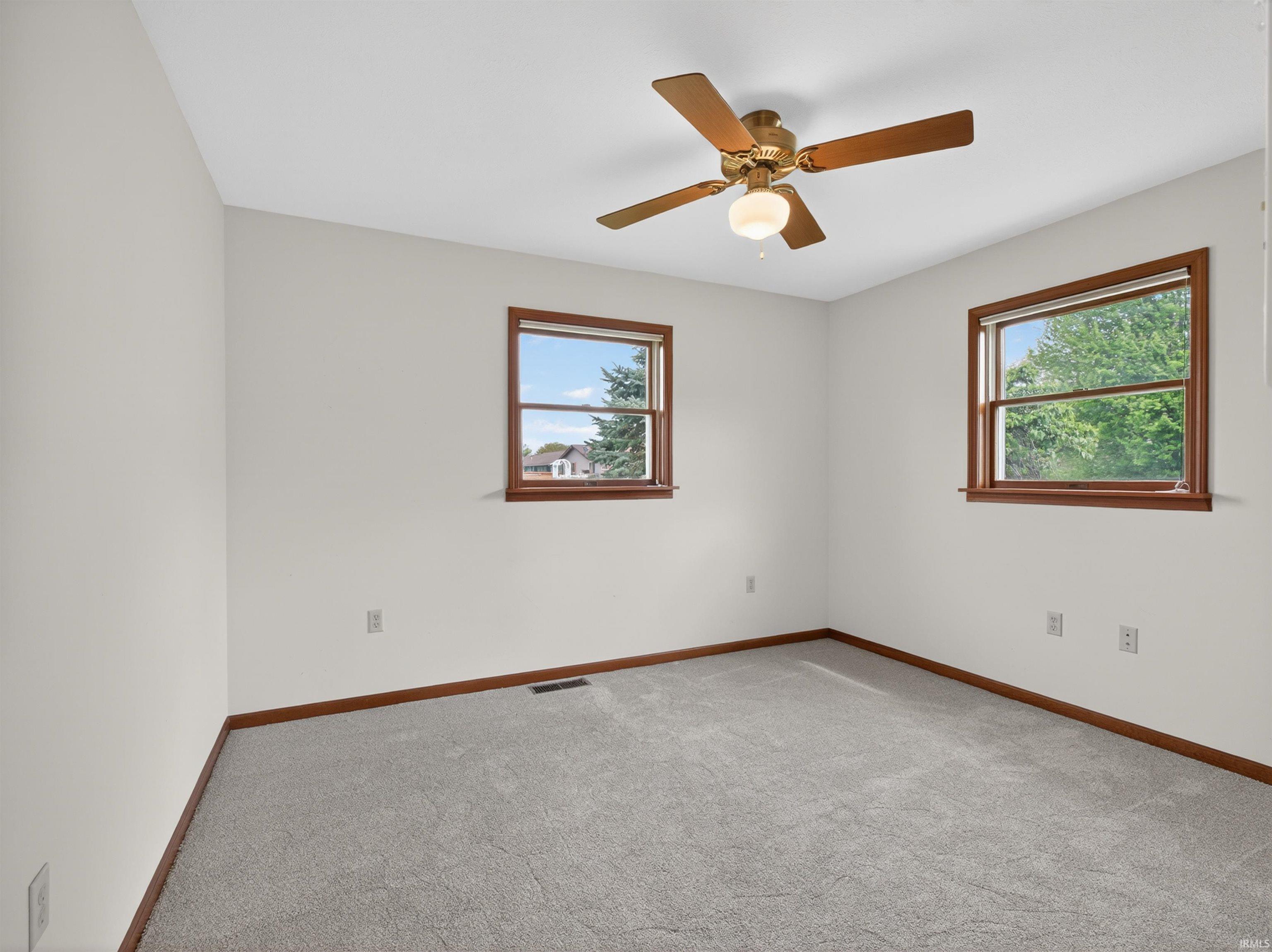 Bright room featuring two windows with wood-finish trim, a ceiling fan with integrated lighting, and light grey carpeting