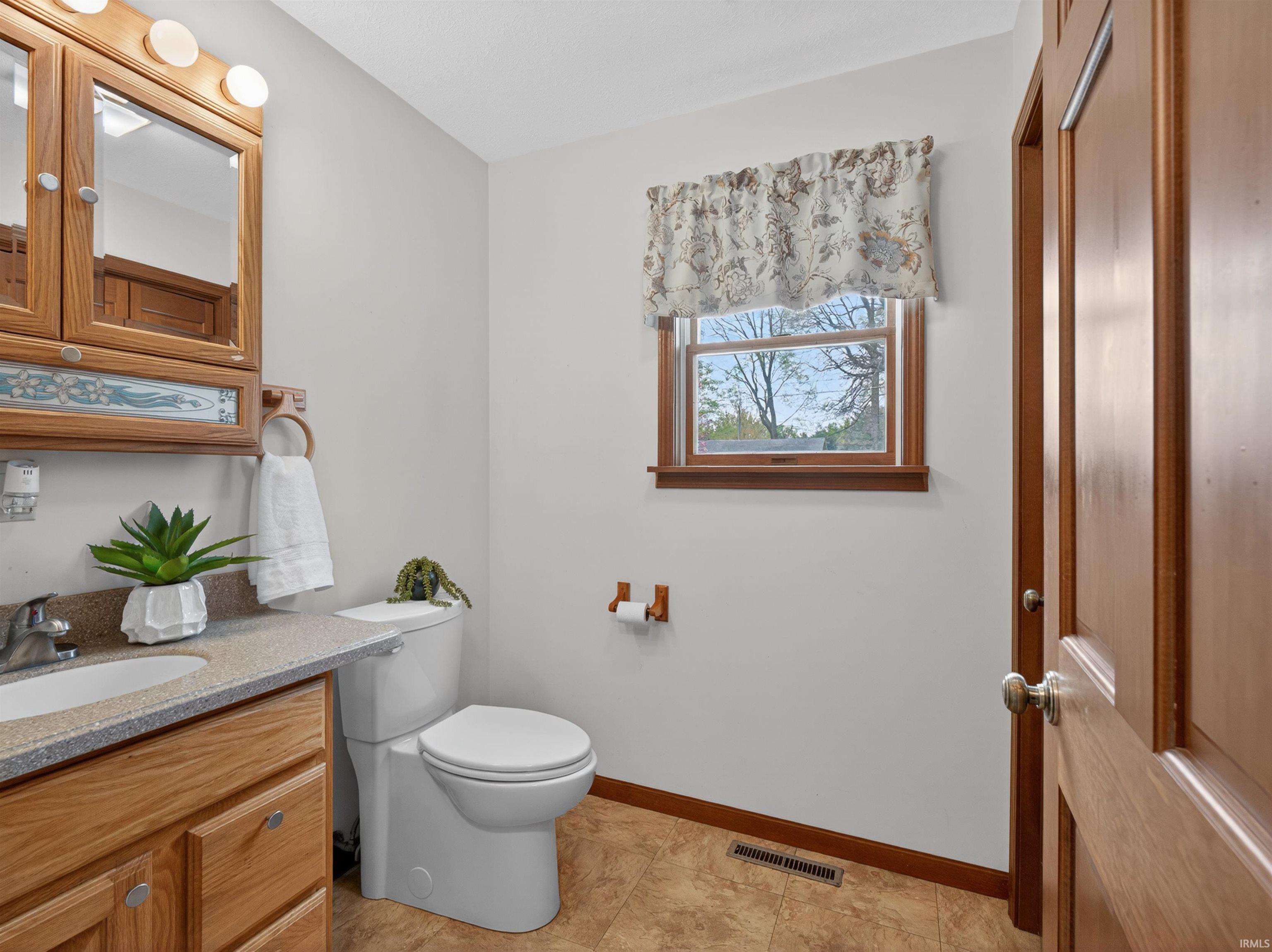 Bathroom featuring a wood-finish vanity with a built-in sink, a speckled countertop, and an overhead mirrored medicine cabinet with integrated lighting