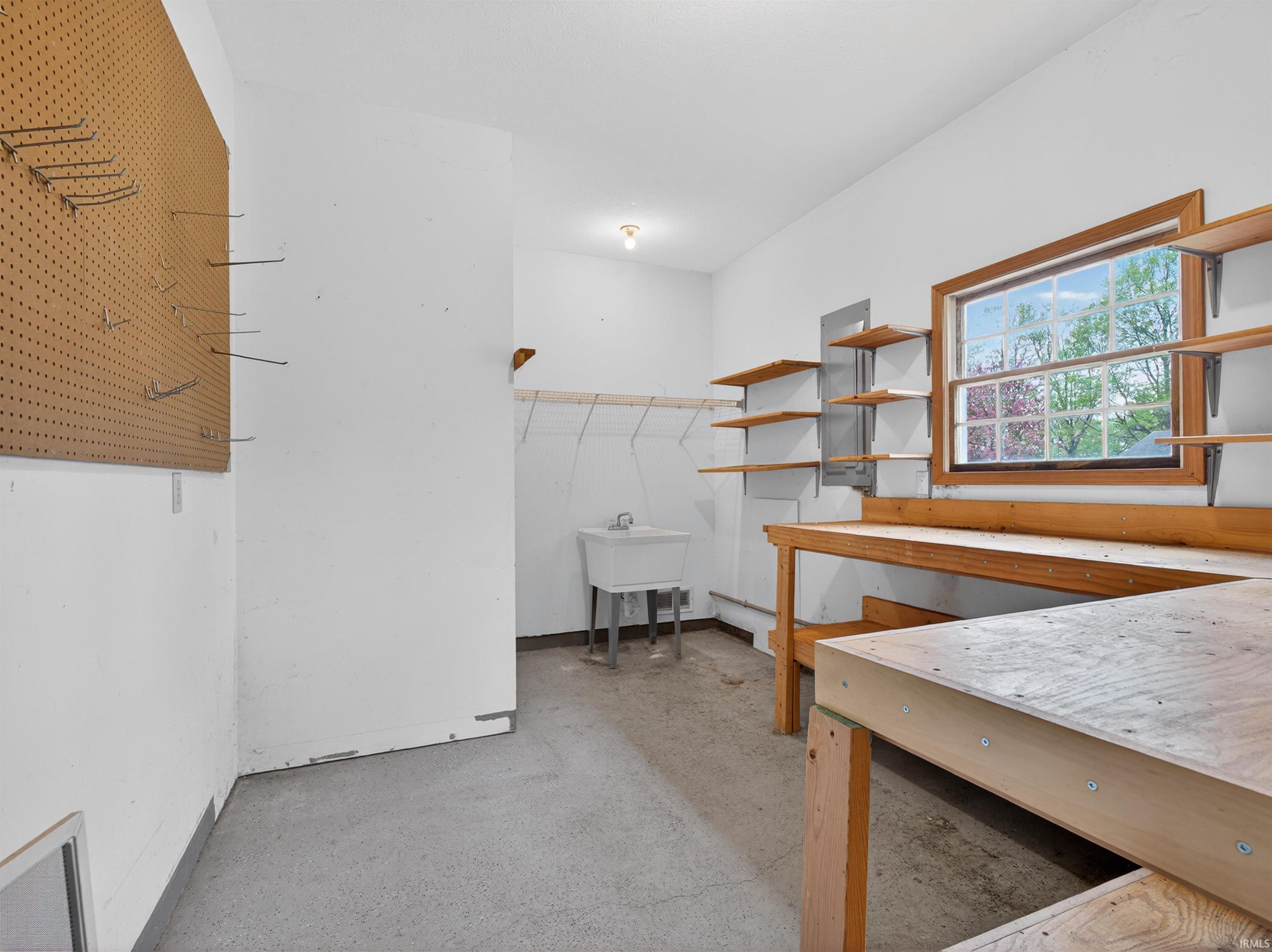 Utility room featuring a built-in workbench, wall-mounted shelving, a utility sink, and a pegboard storage system