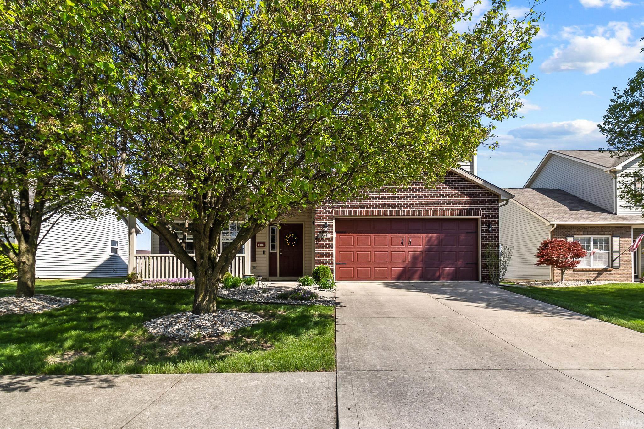 Brick and siding exterior featuring an attached garage, covered front porch, concrete driveway, and mature landscaping