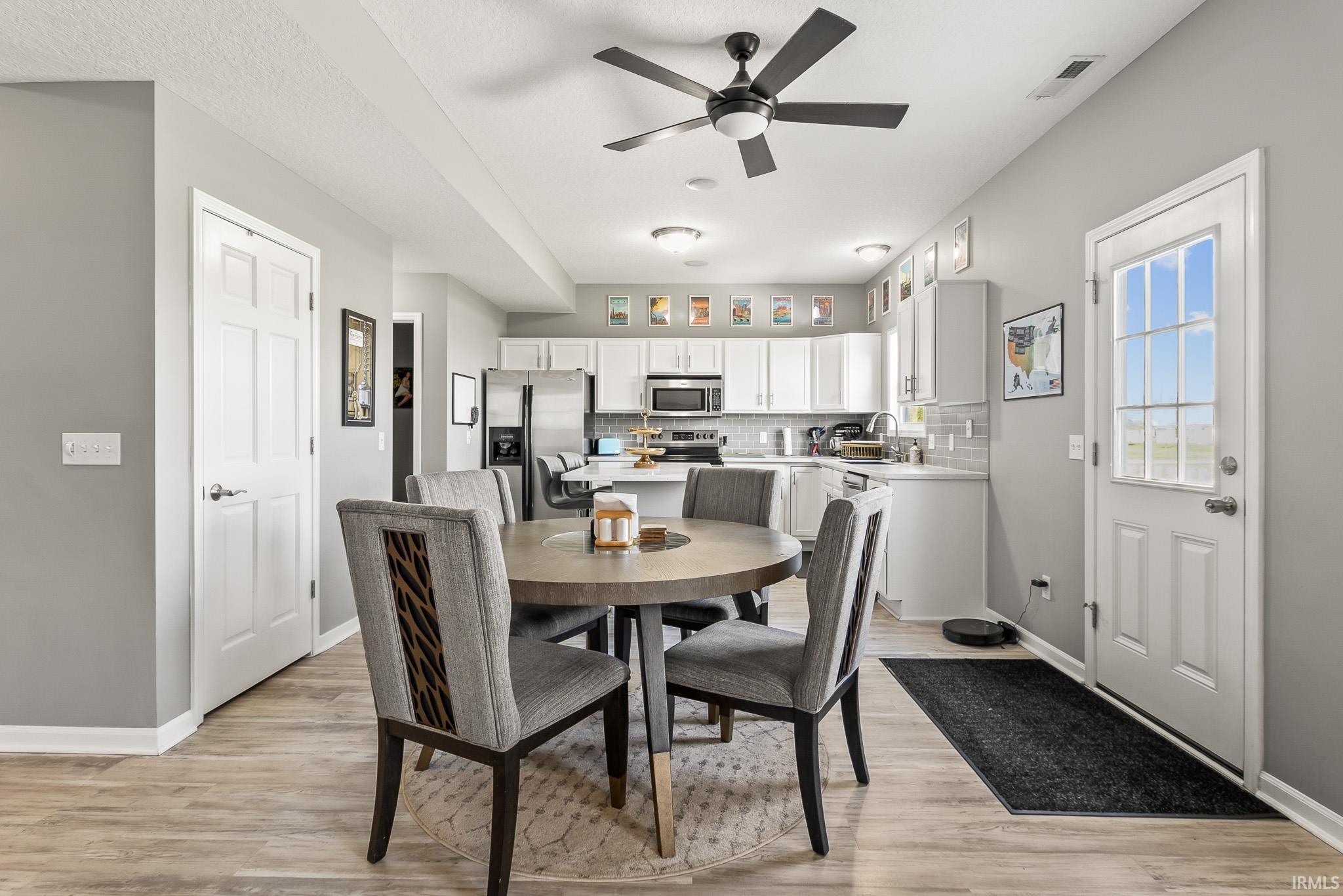 Open-concept kitchen and dining area featuring wood-finish flooring, white cabinetry, stainless steel appliances, a ceiling fan, and a paneled exterior door with glass inserts
