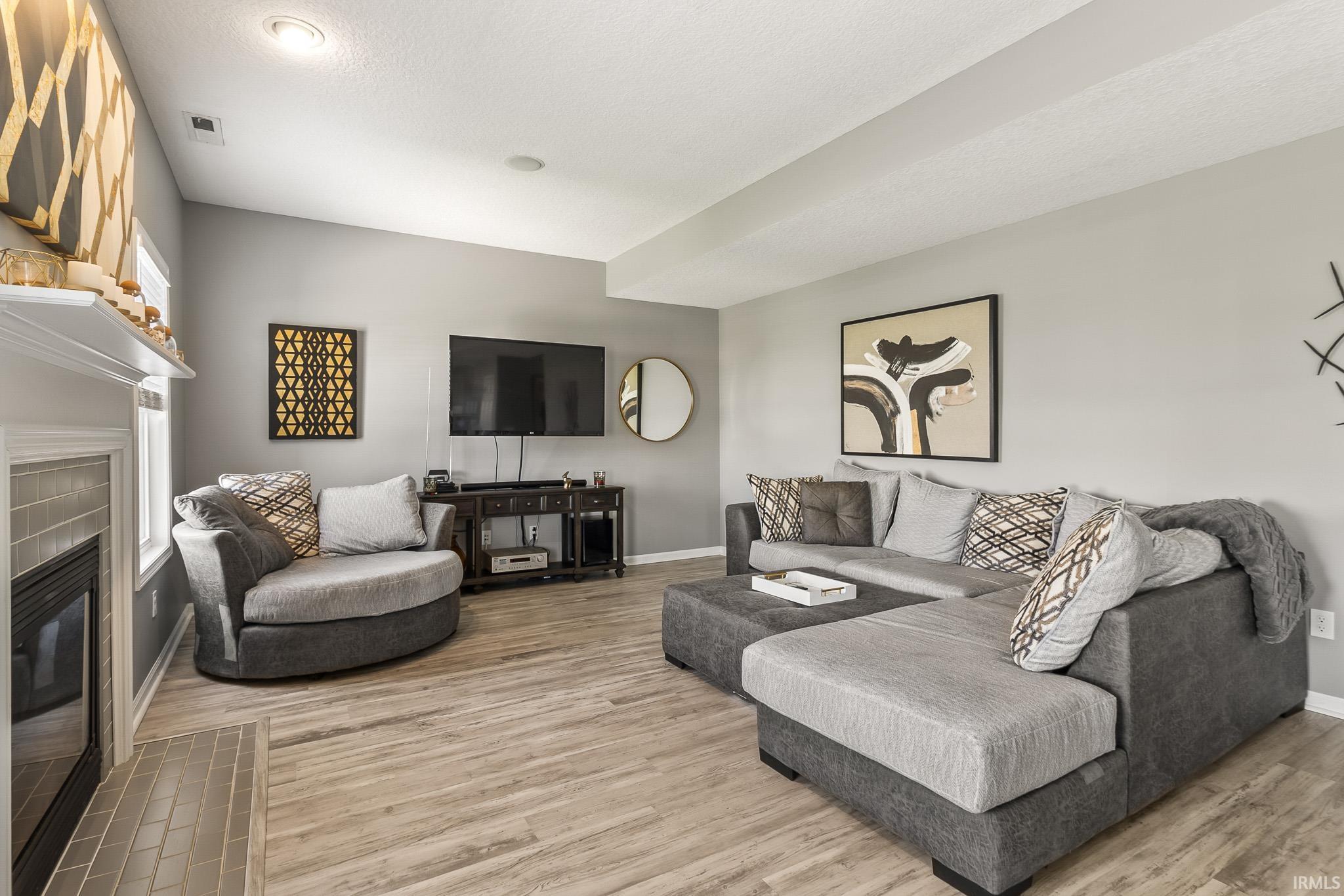 Spacious living area featuring light wood-finish flooring, a tiled fireplace with white mantel, a recessed ceiling light, and neutral wall tones