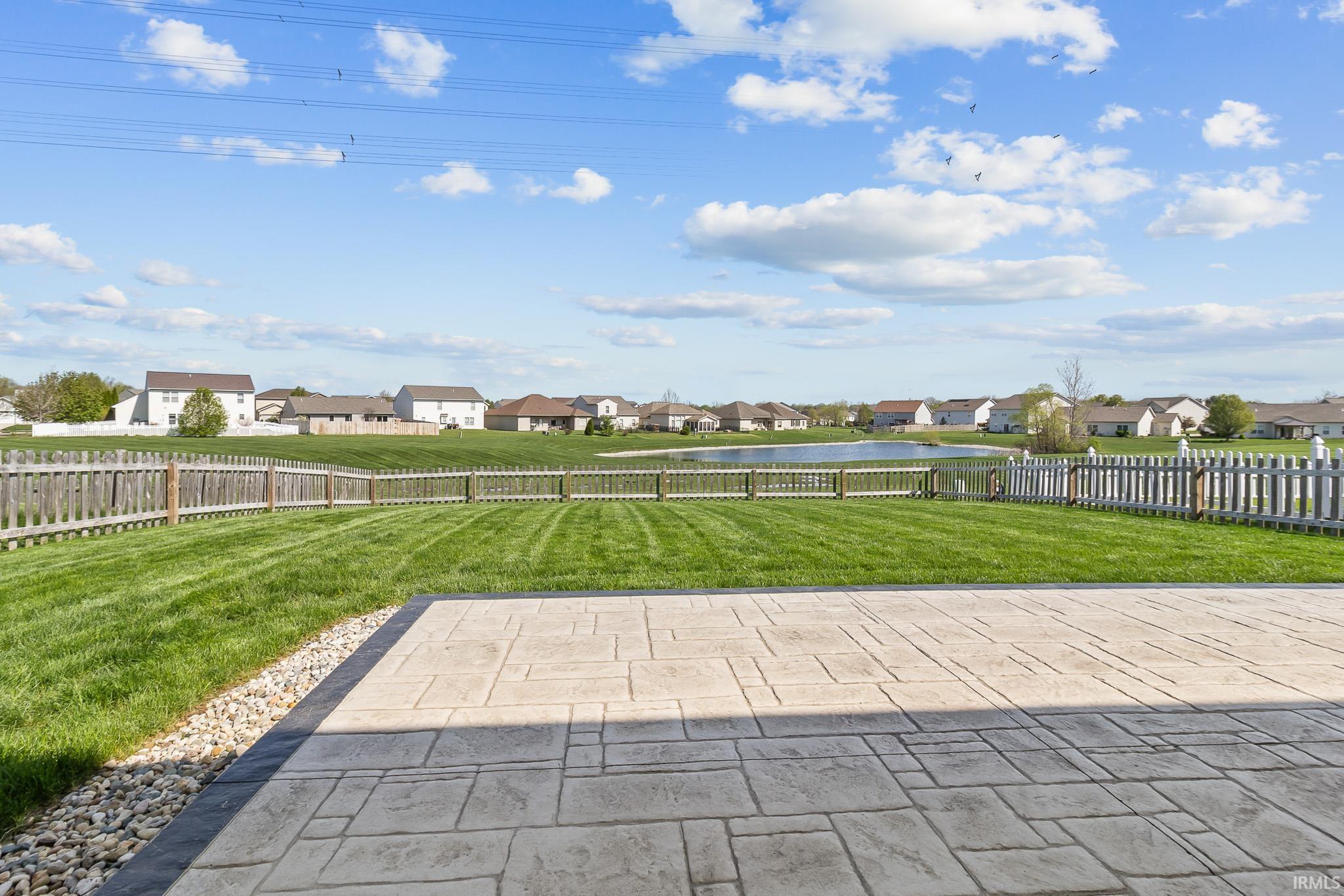 Expansive backyard featuring a stamped concrete patio, manicured lawn, and a perimeter fence