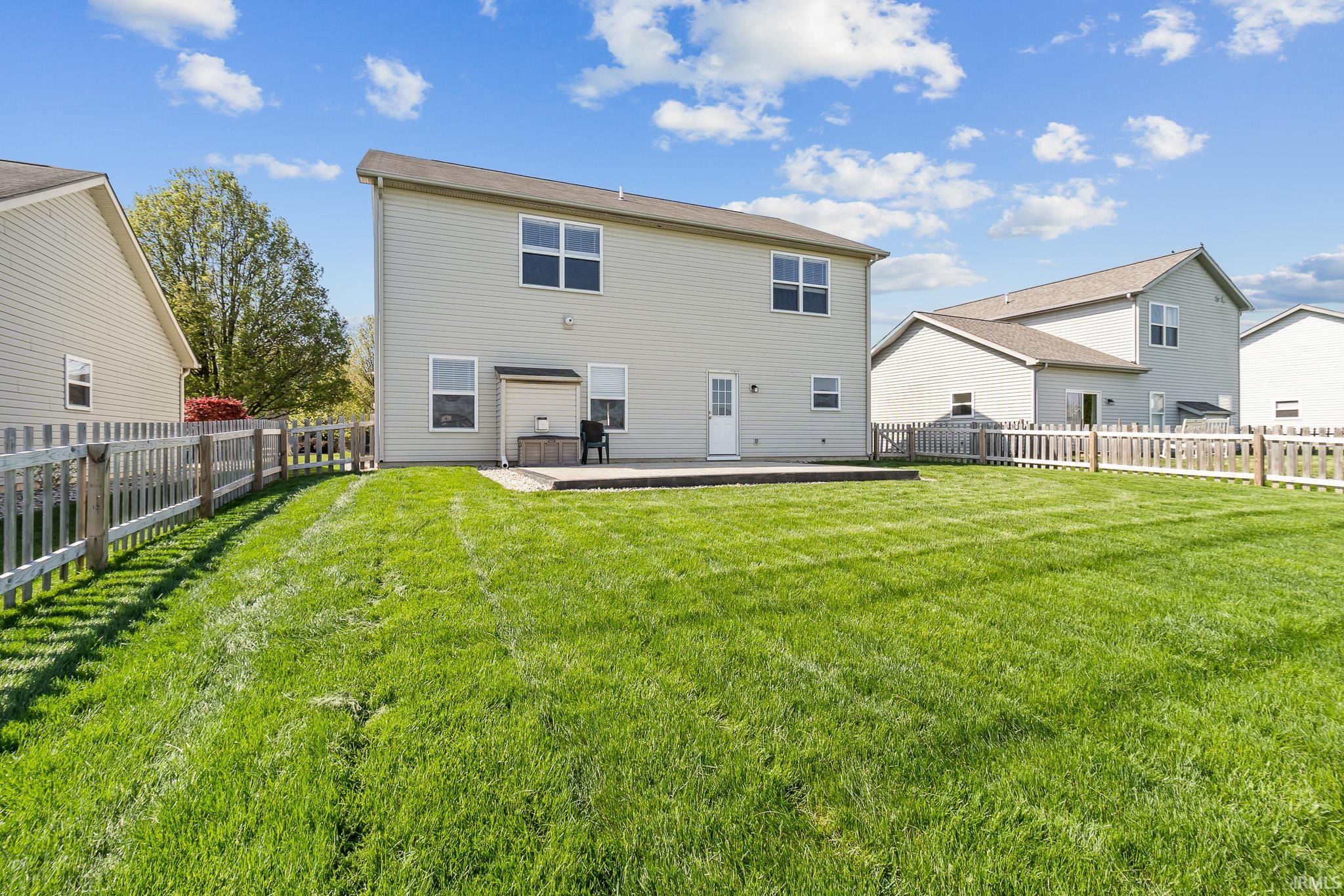 Expansive green lawn with a white picket fence, featuring a concrete patio and light-toned siding on the dwelling