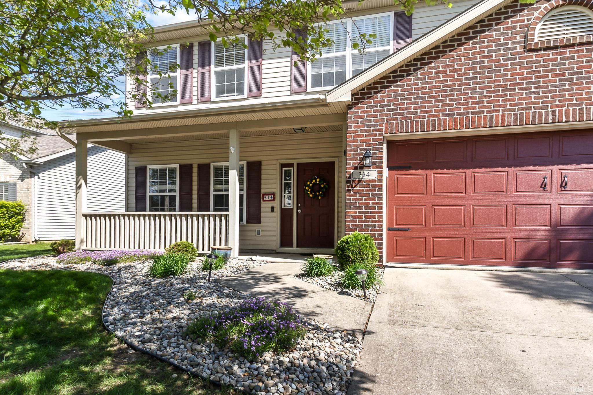 Two-story residence featuring a covered front porch, a red brick facade, and tan siding