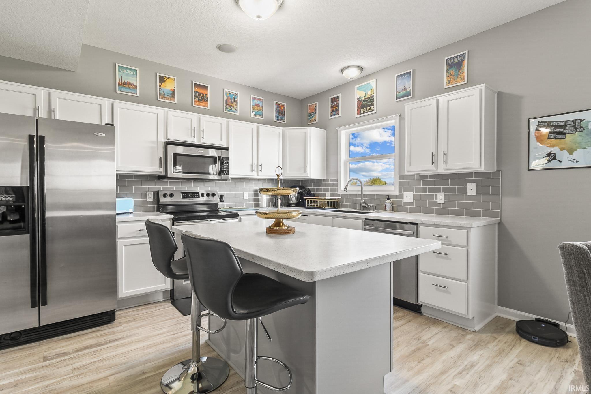 Kitchen featuring a central island with countertop seating, white cabinetry, stainless steel appliances, a subway tile backsplash, and wood-finish flooring