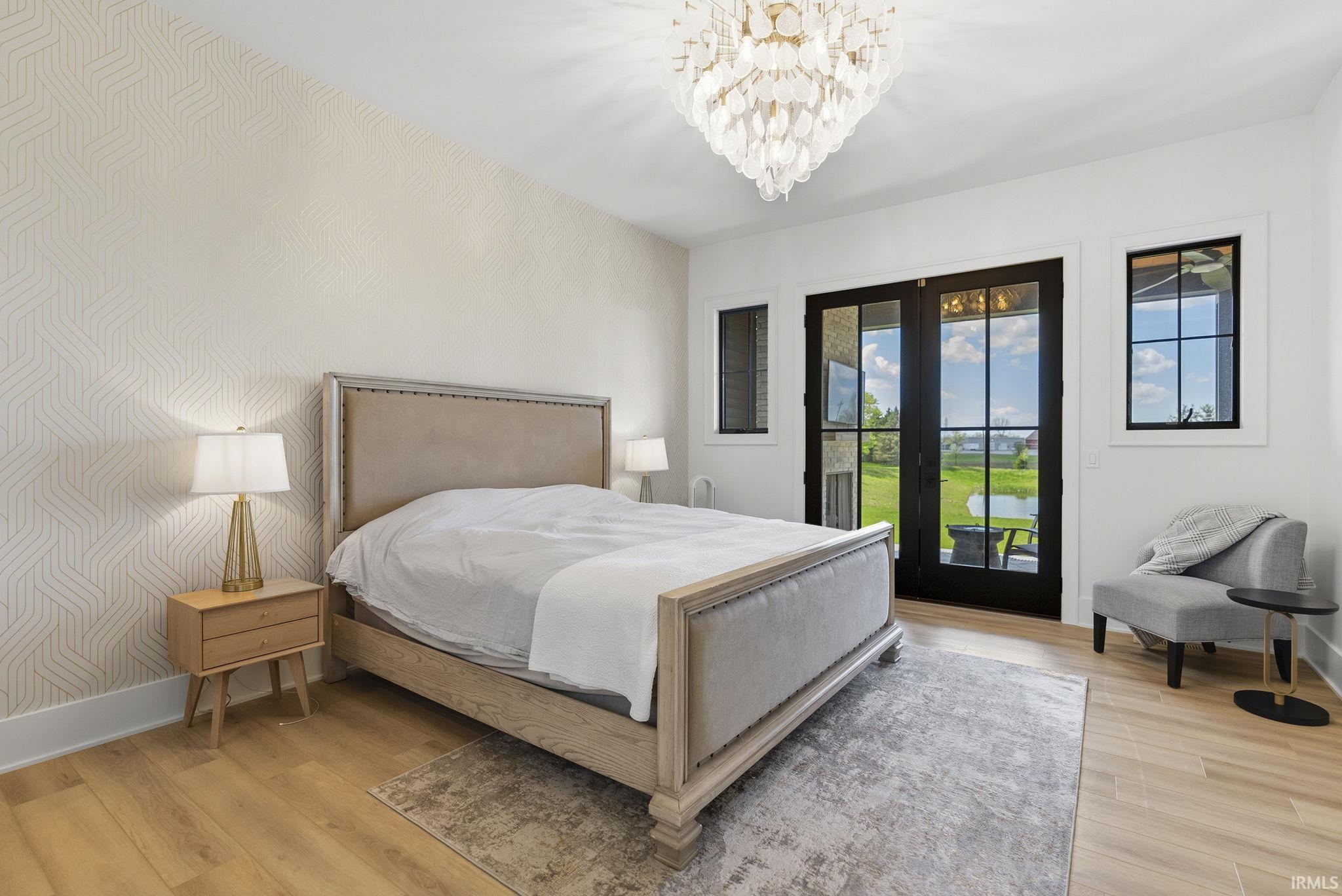 Room featuring wood-finish flooring, a contemporary chandelier, patterned accent wall, and double glass-paneled doors opening to an exterior patio