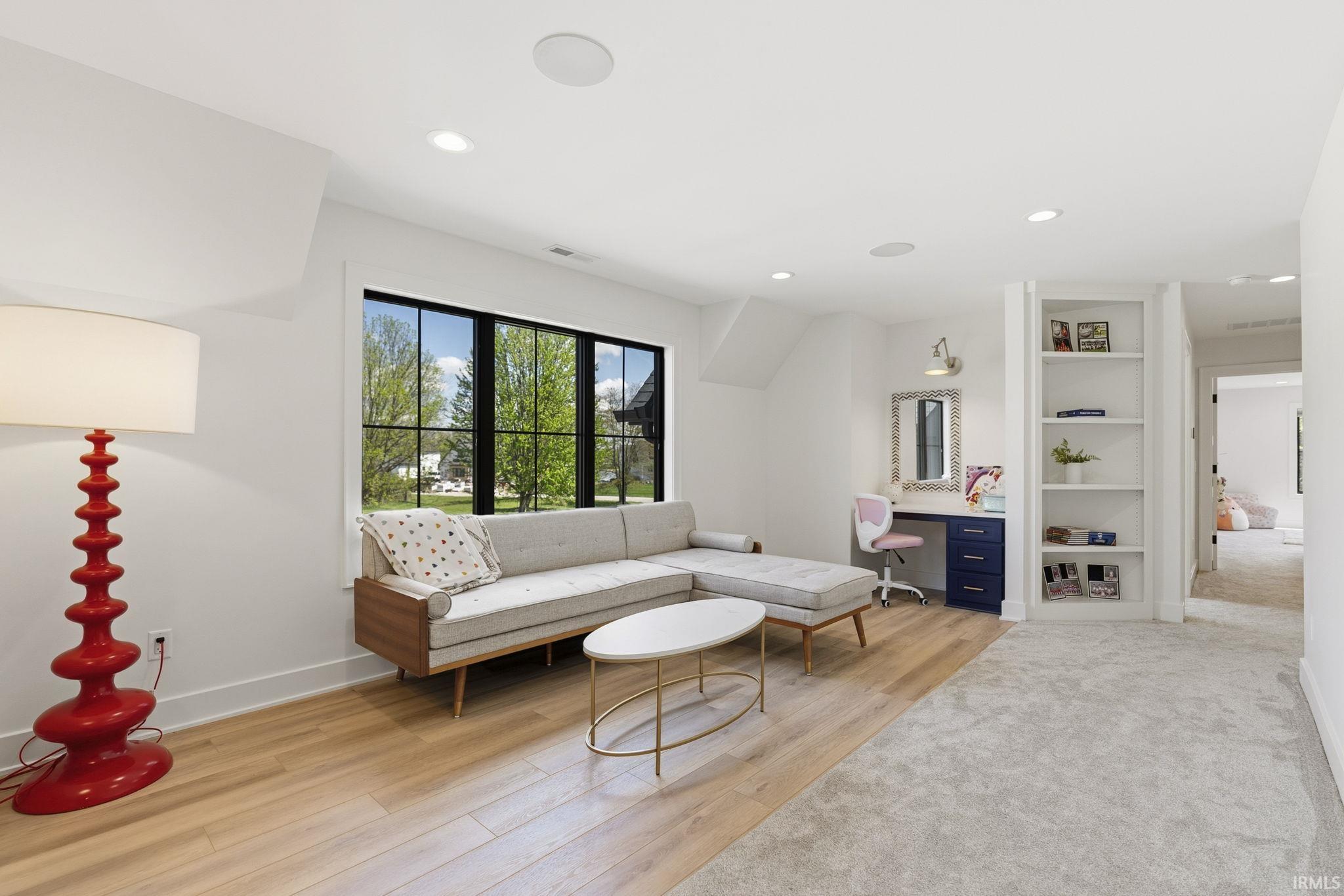 Spacious room featuring a large window with black framing, wood-finish flooring, built-in shelving, recessed lighting, and a neutral carpeted area