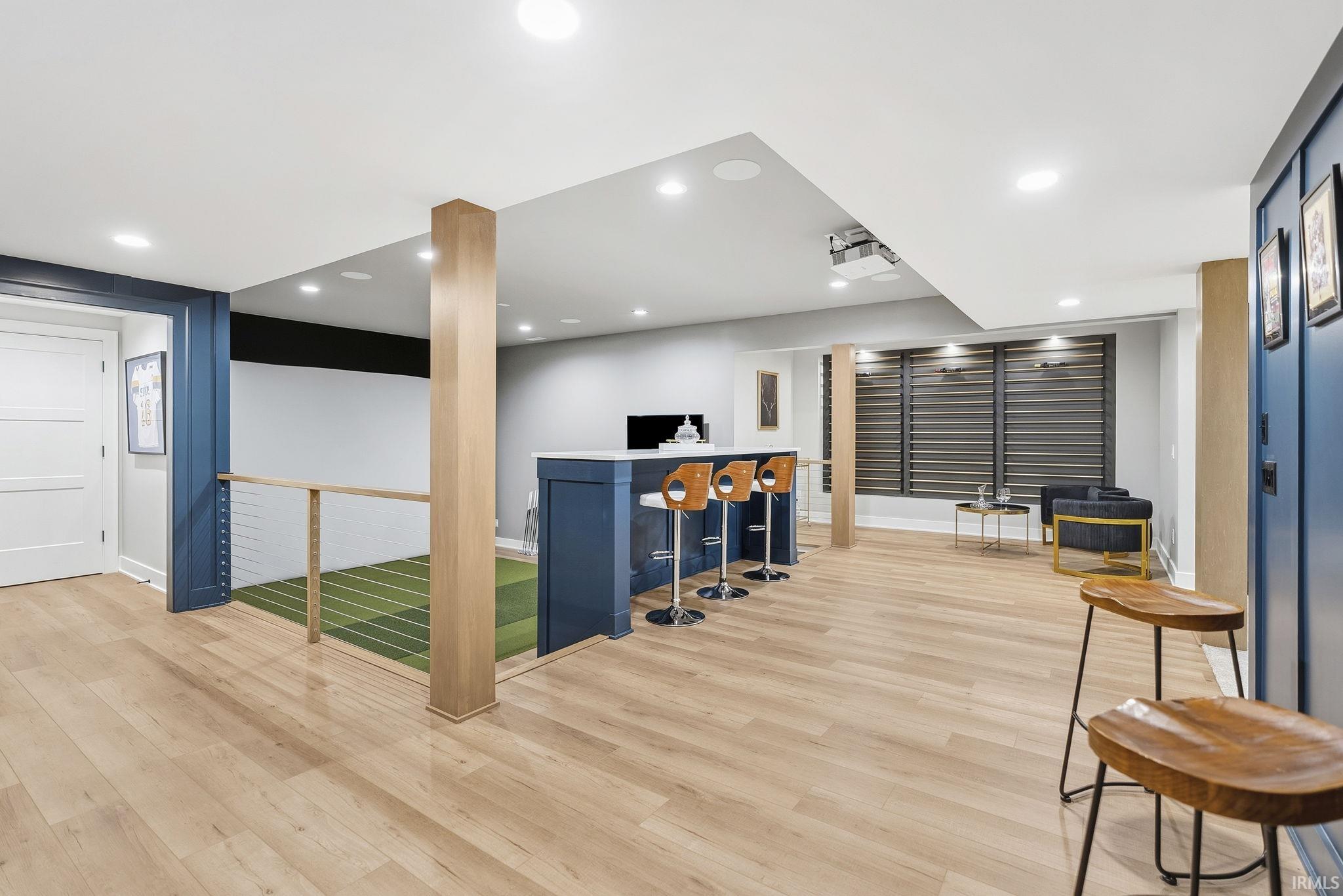 Spacious entertainment area featuring wood-finish flooring, a built-in bar with a light-toned countertop, recessed lighting, and a cable railing system
