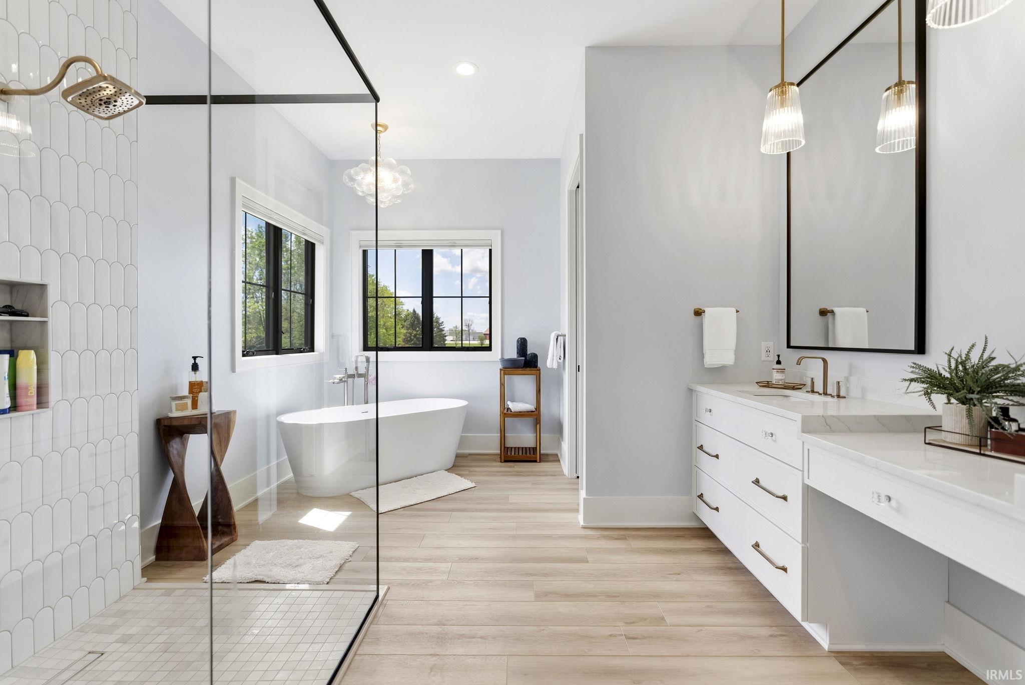 Spacious bathroom featuring a frameless glass shower enclosure with decorative tile, a standalone soaking tub, and black-framed windows