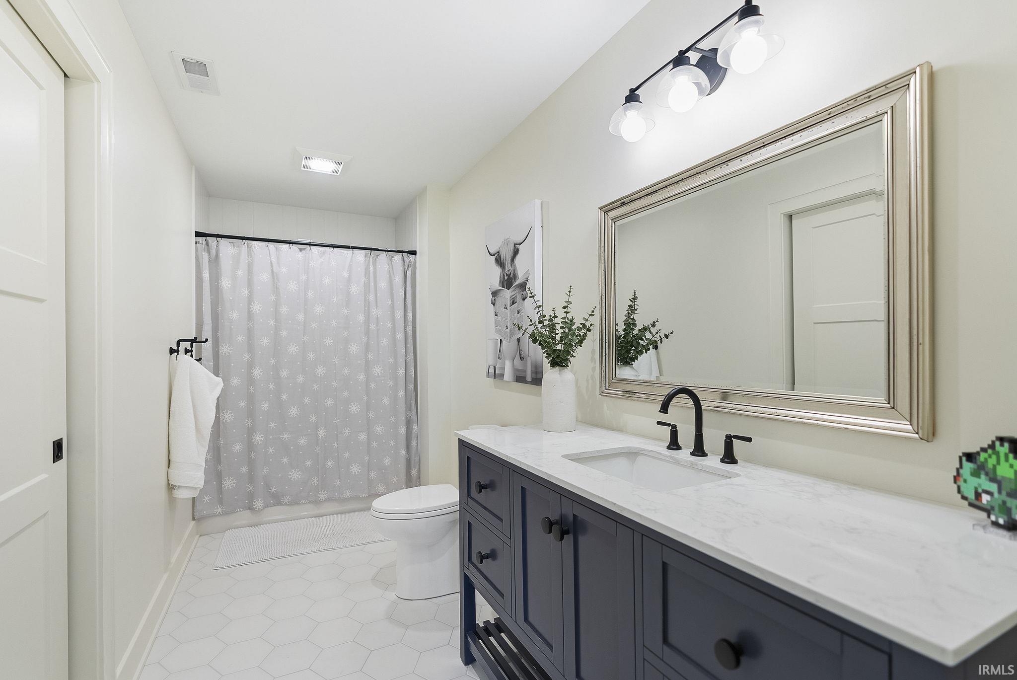 Bathroom featuring a dark blue vanity with a white countertop and undermount sink, matte black faucet, and a large framed mirror