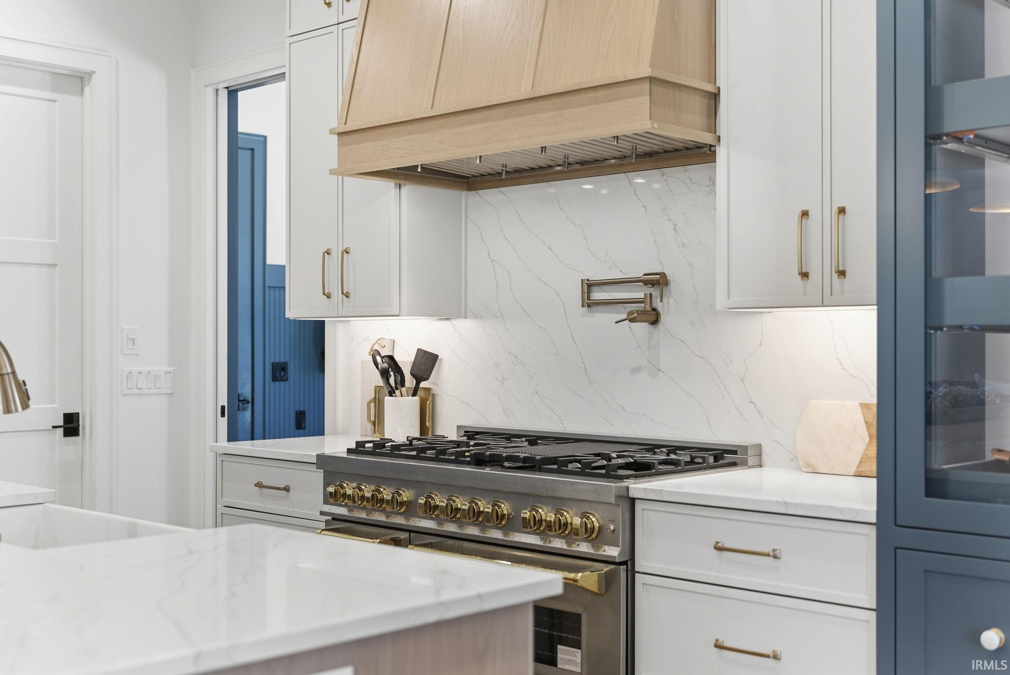 Gourmet kitchen featuring a professional-grade range, custom wood hood, full-height veined slab backsplash, under-cabinet lighting, and a pot filler