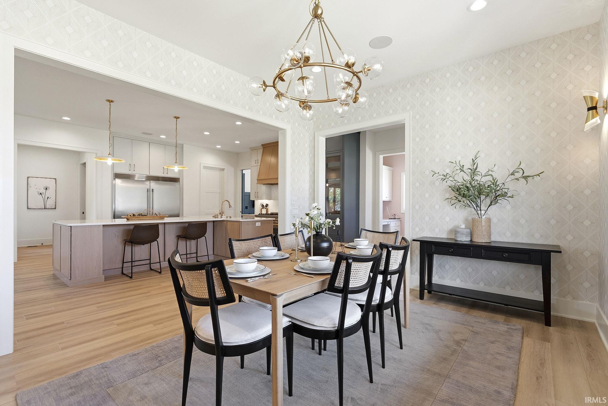 Open-concept dining area featuring a contemporary chandelier, patterned wallpaper, and light wood-finish flooring