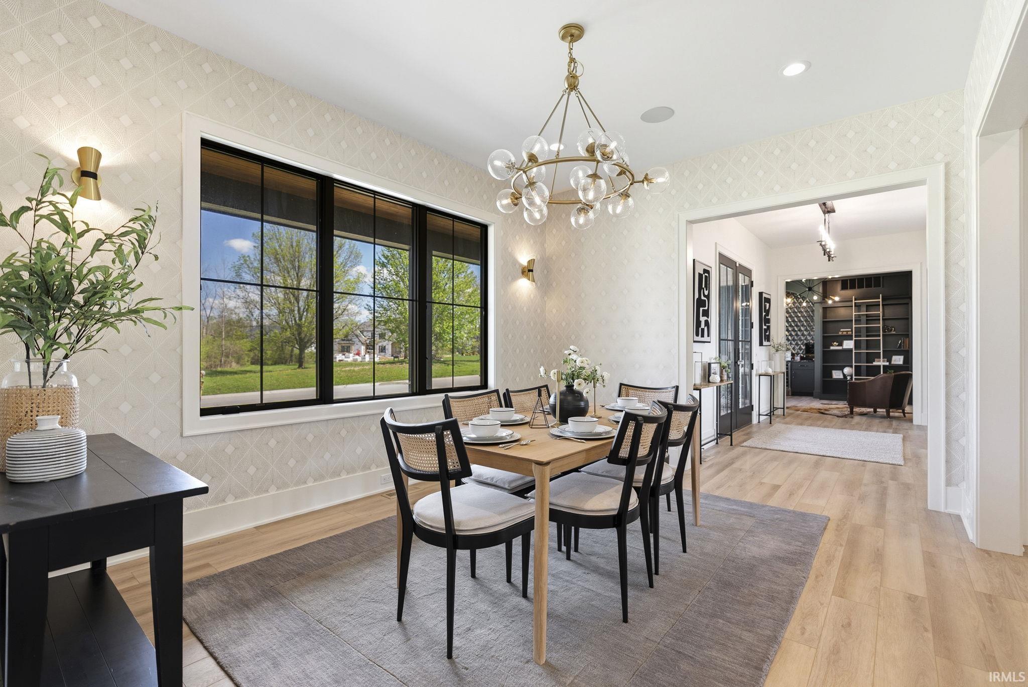 Dining area featuring a large picture window with black grid panes, wood-finish flooring, and patterned wall covering