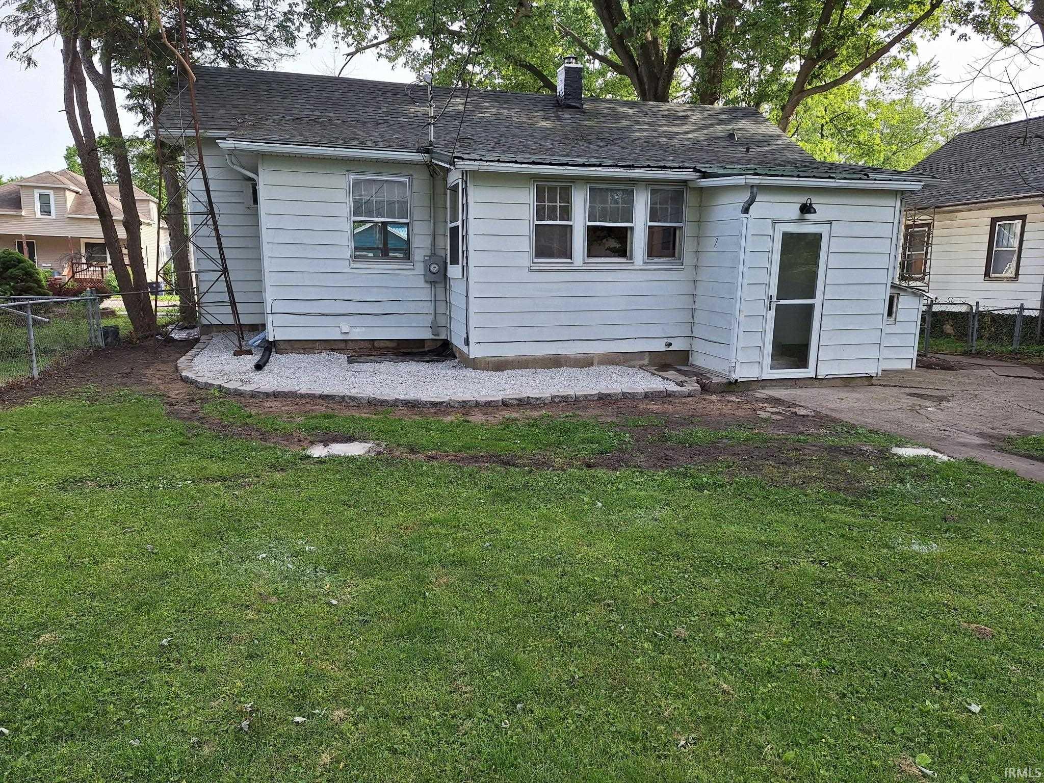 Rear exterior featuring white horizontal siding, a gravel patio area with stone edging, and a detached screened door entry