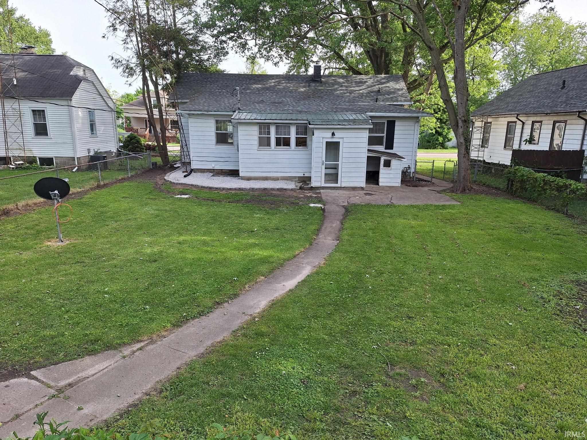 Rear exterior featuring white siding, a partial concrete patio, and a concrete pathway extending through a grass lawn
