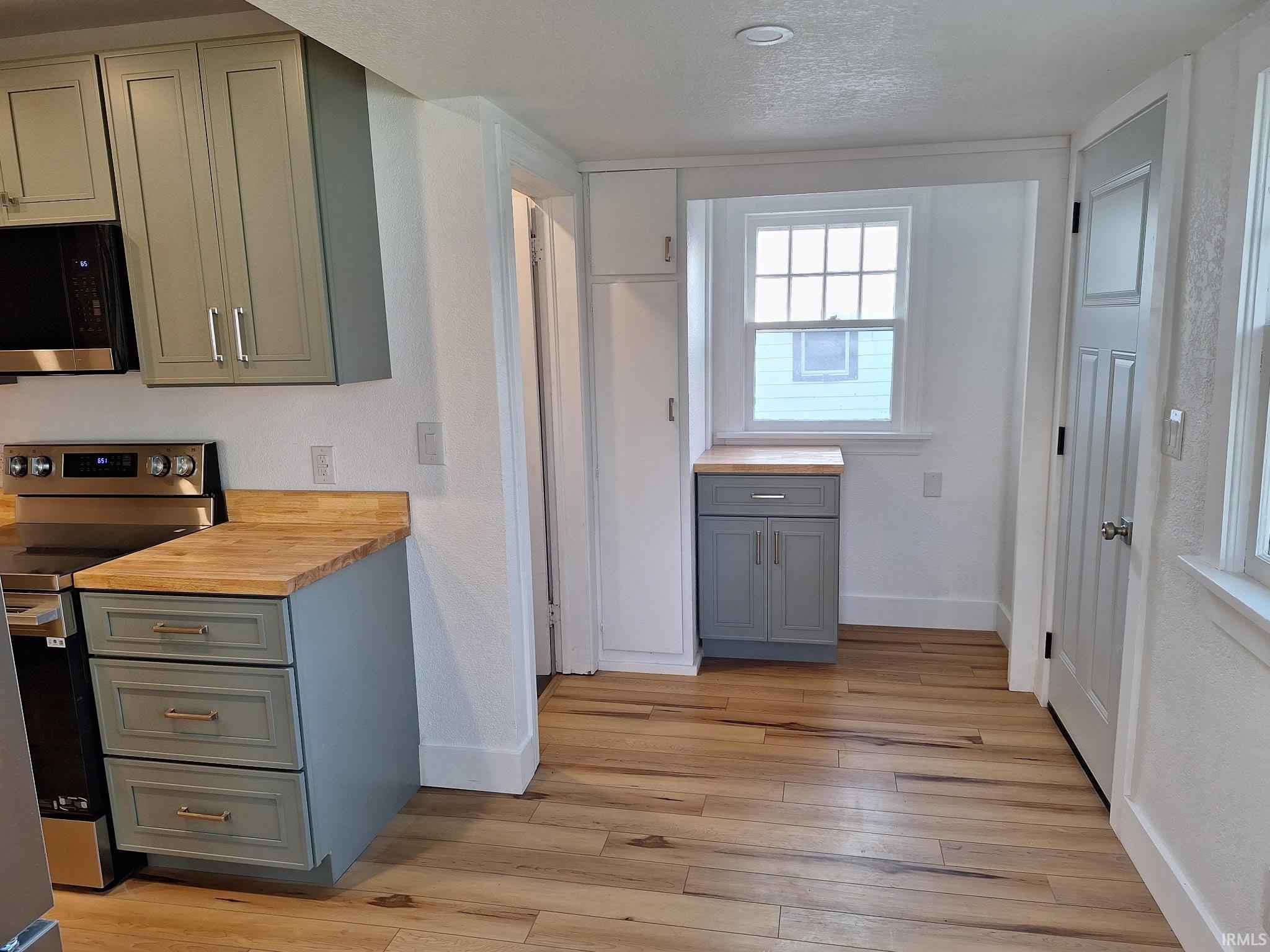 Kitchen featuring wood-finish flooring, two-tone cabinetry with gold-tone hardware, wood countertops, and stainless steel appliances