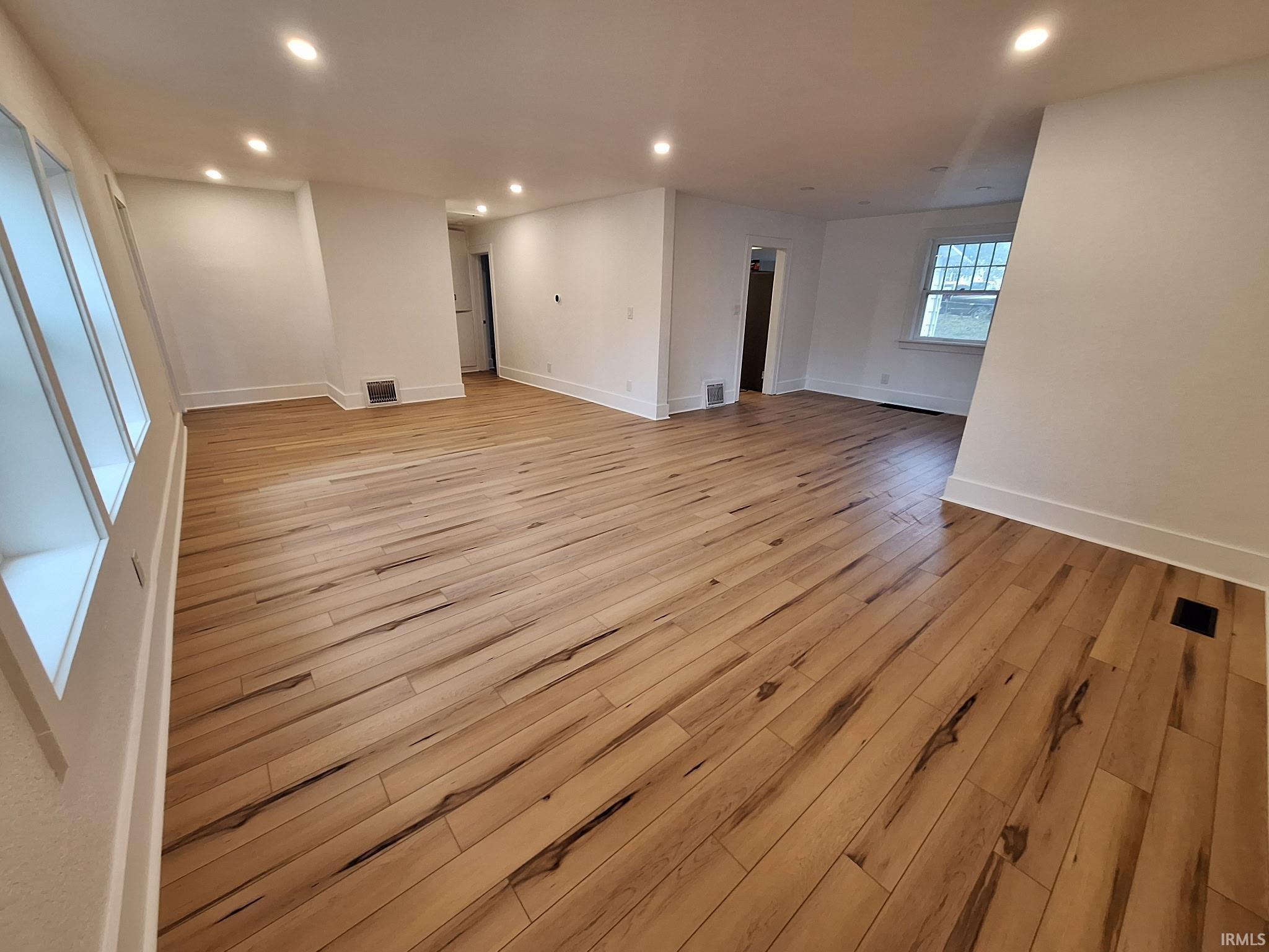 Spacious room featuring wide plank wood-finish flooring, recessed lighting, multiple windows, white walls, and white baseboards