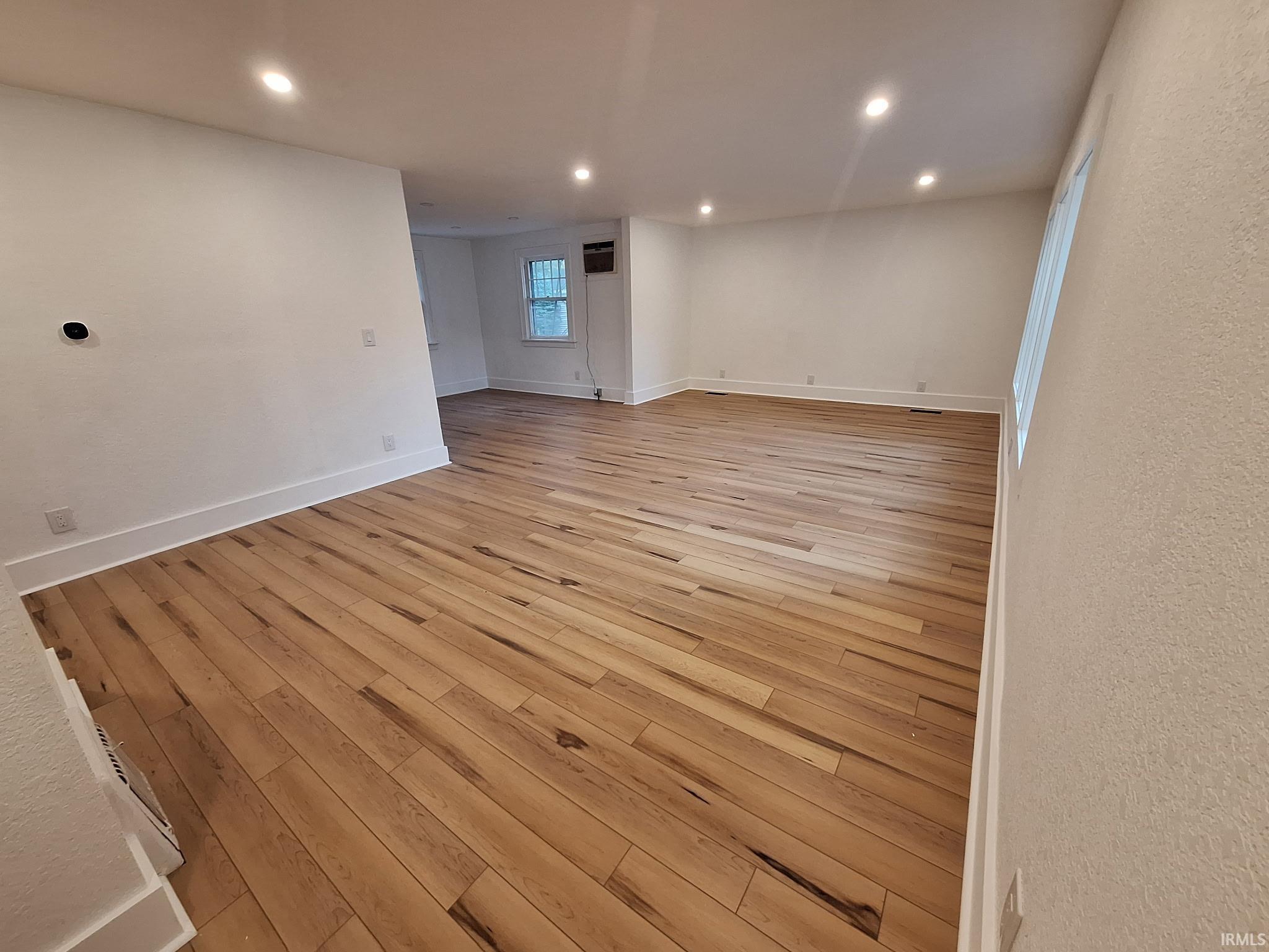 Spacious room featuring light wood-finish flooring, recessed lighting, white baseboards, and textured white walls