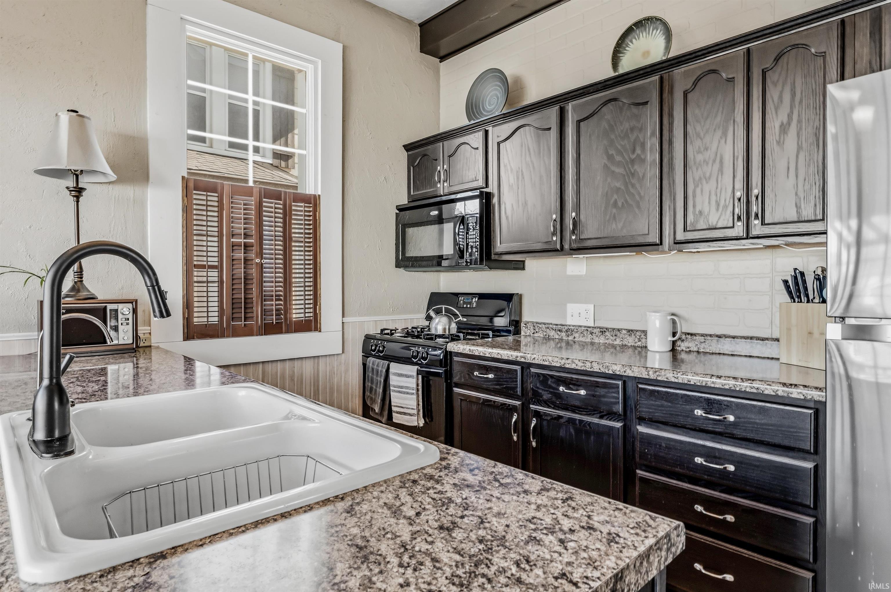 Kitchen with black appliances, a wainscoted wall, light countertops, and dark wood finish cabinetry