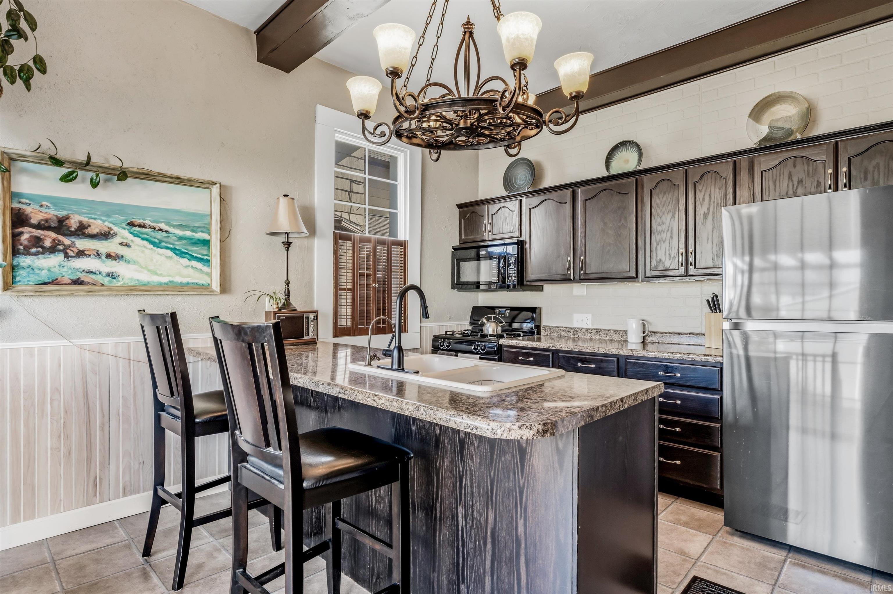 Kitchen with dark wood finish cabinets, black appliances, a wainscoted wall, a breakfast bar, and suspended lighting