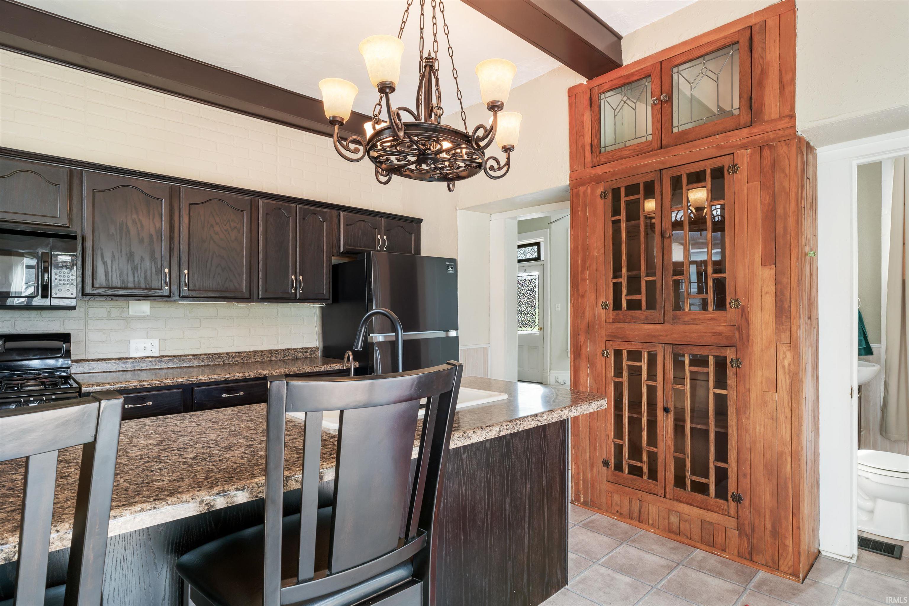 Kitchen featuring dark wood-finish cabinetry, light-toned subway tile backsplash, and a breakfast bar with stone-finish countertops