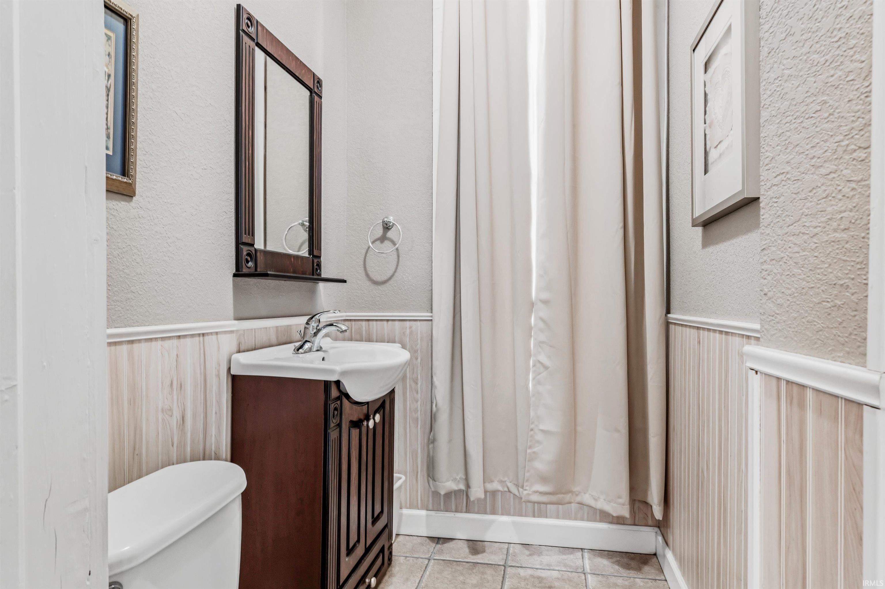 Bathroom with a textured wall, vanity, and a wainscoted wall