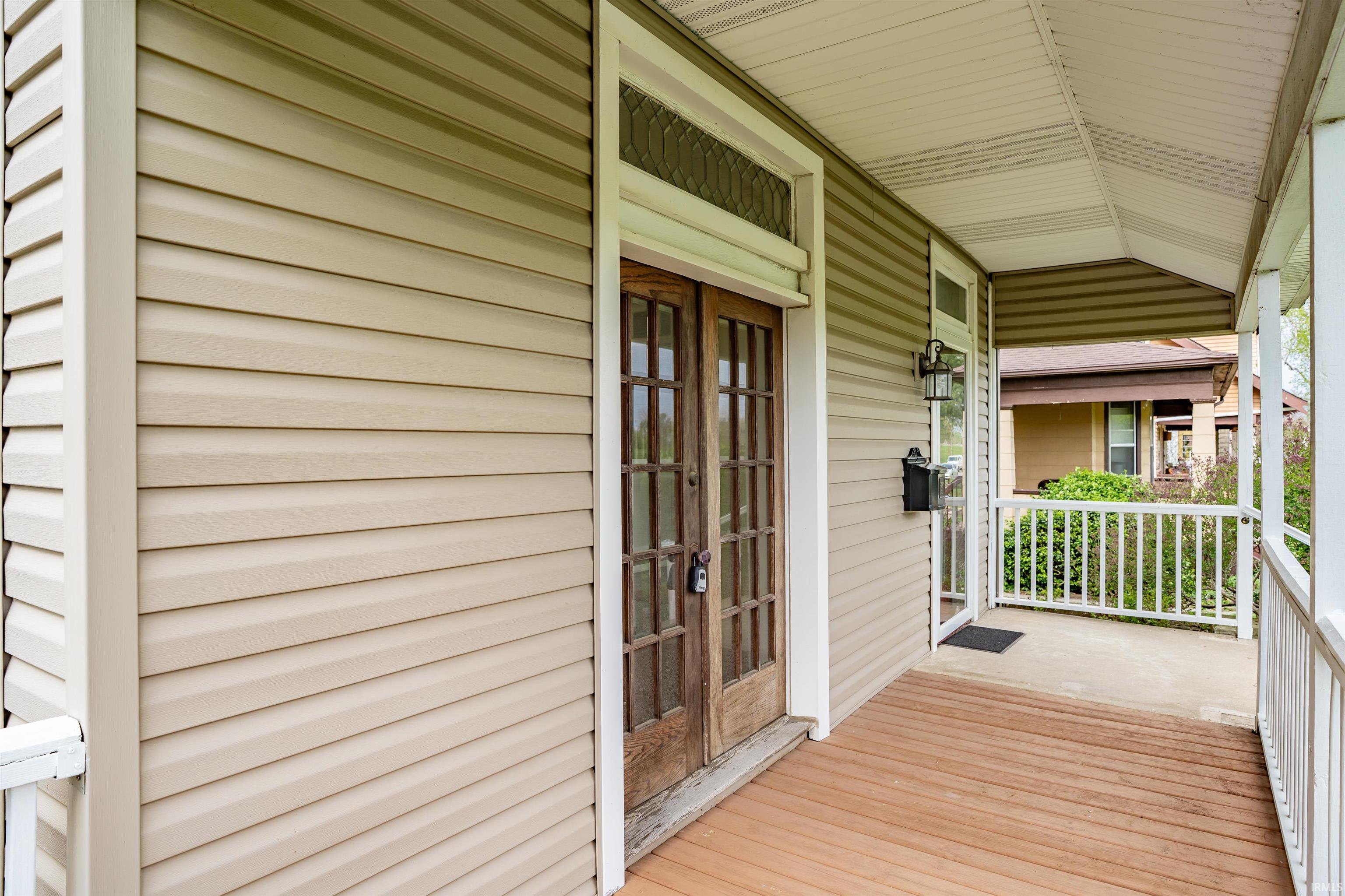 Covered front porch featuring wood-finish flooring, white railing, and a beadboard ceiling