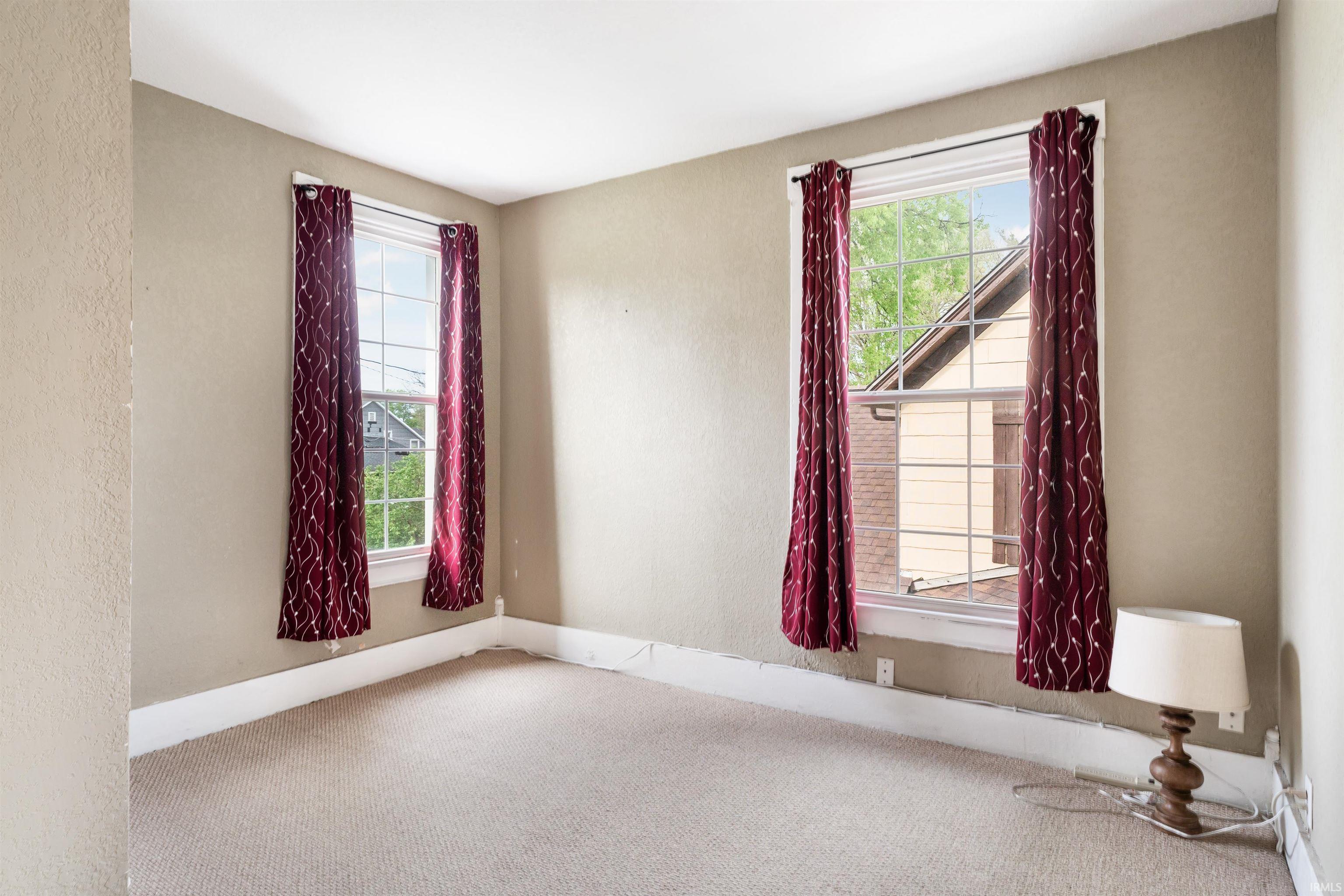 Carpeted room featuring two large windows with white trim and baseboards