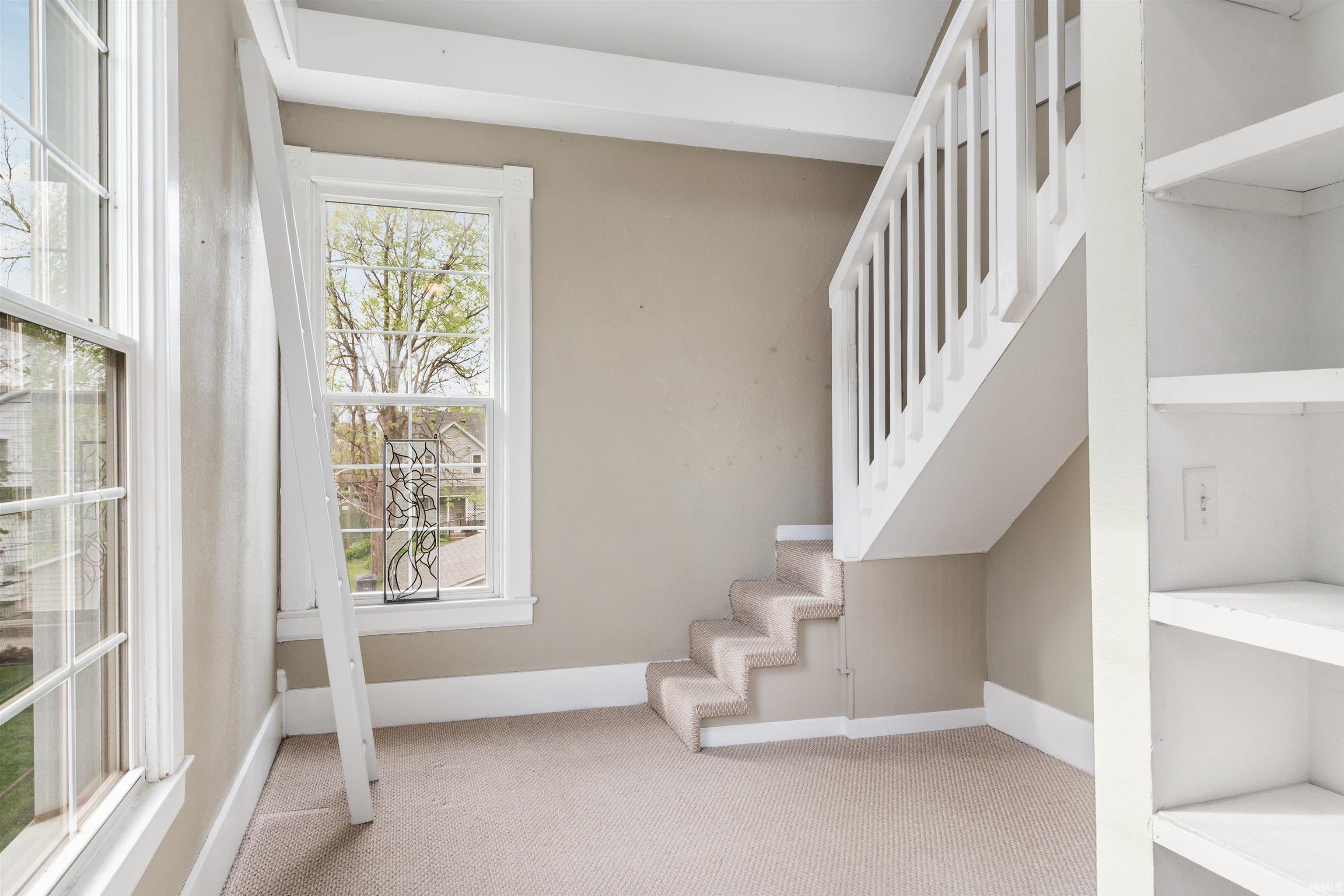 Carpeted staircase with white balusters, built-in shelving, two framed windows, and neutral wall tones