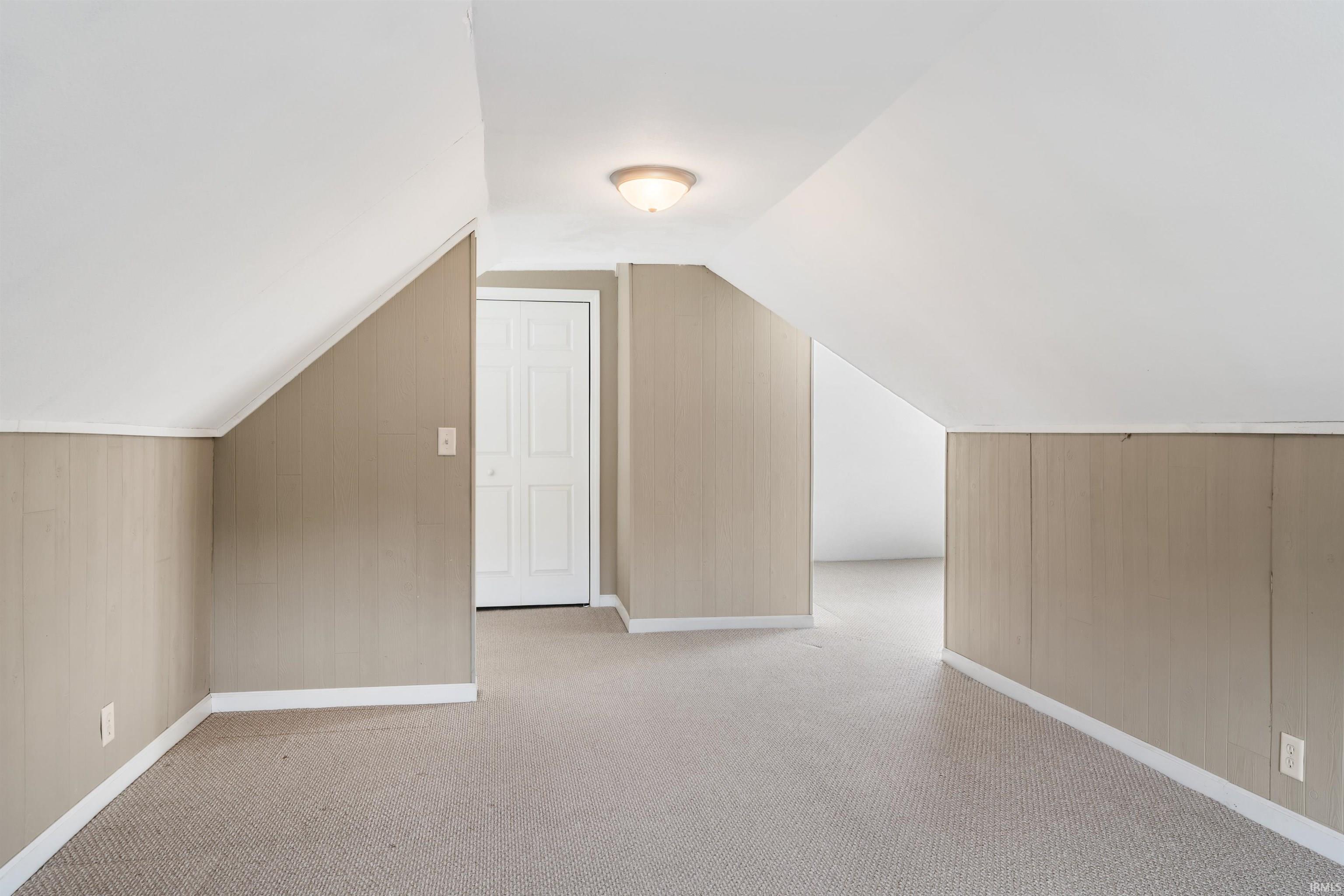 Carpeted room featuring sloped ceilings, beadboard wall paneling, and a flush mount light fixture